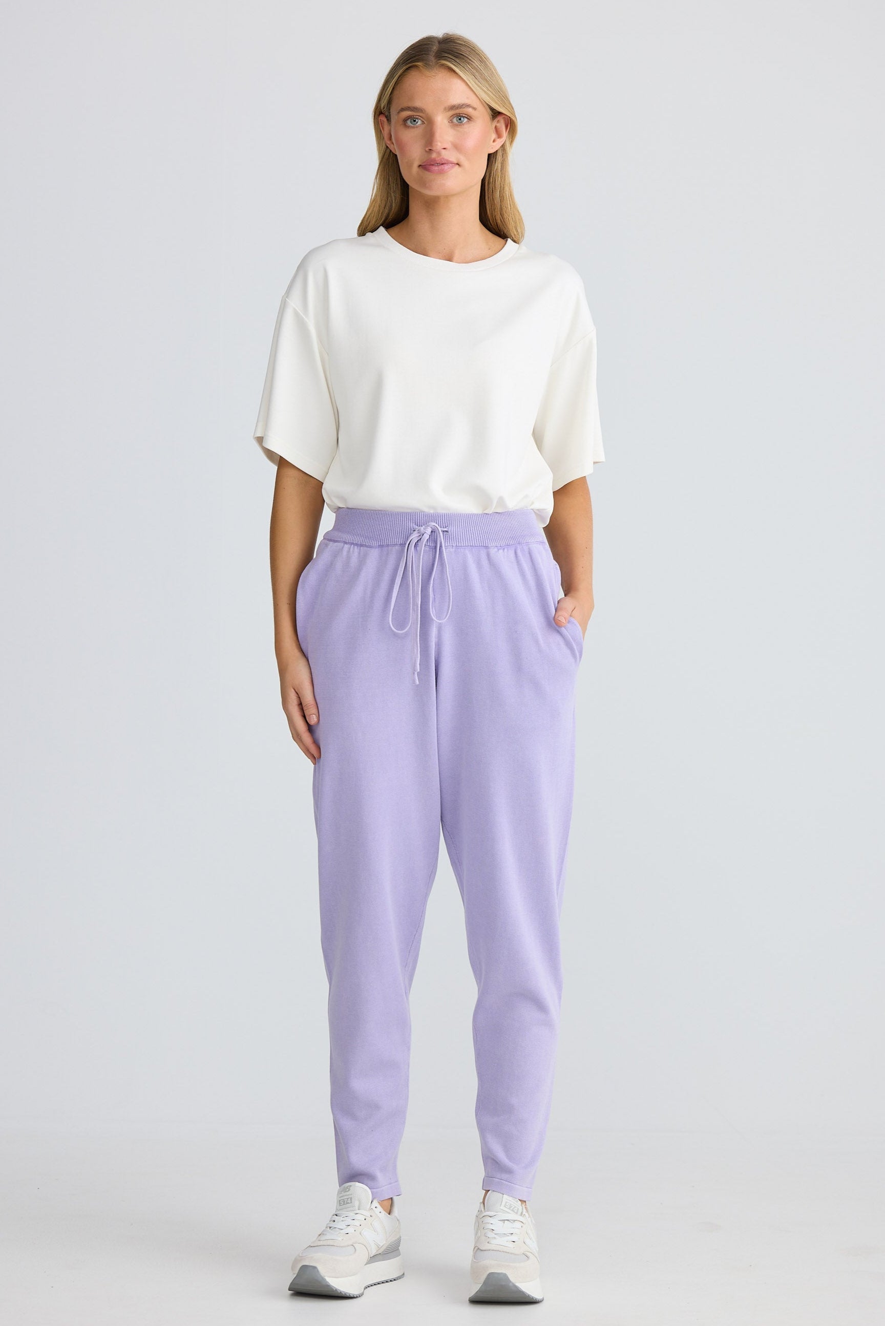 Woman wearing a white top and lavender jogger pants on a plain background