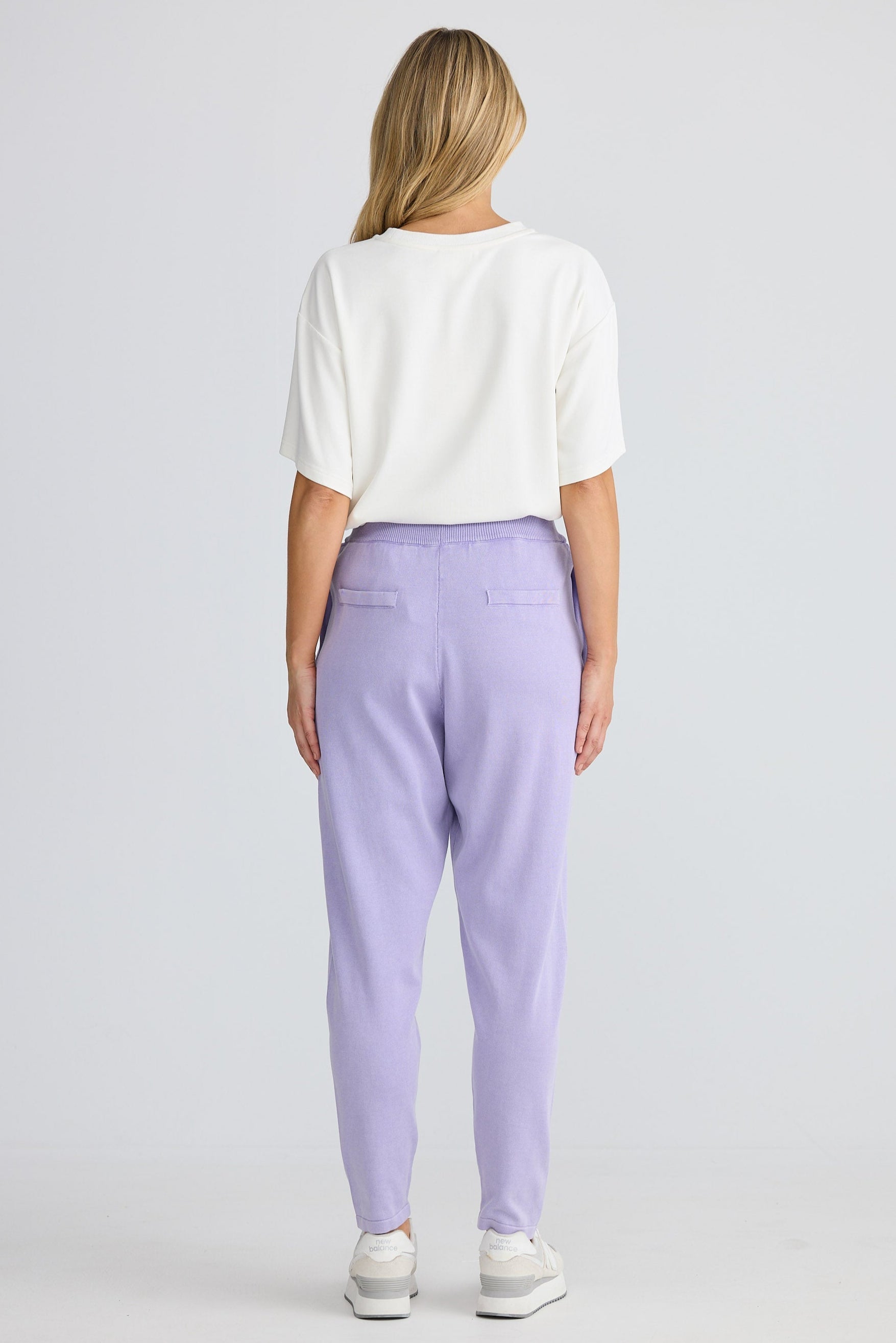 Person wearing a white top and lavender pants on a plain background