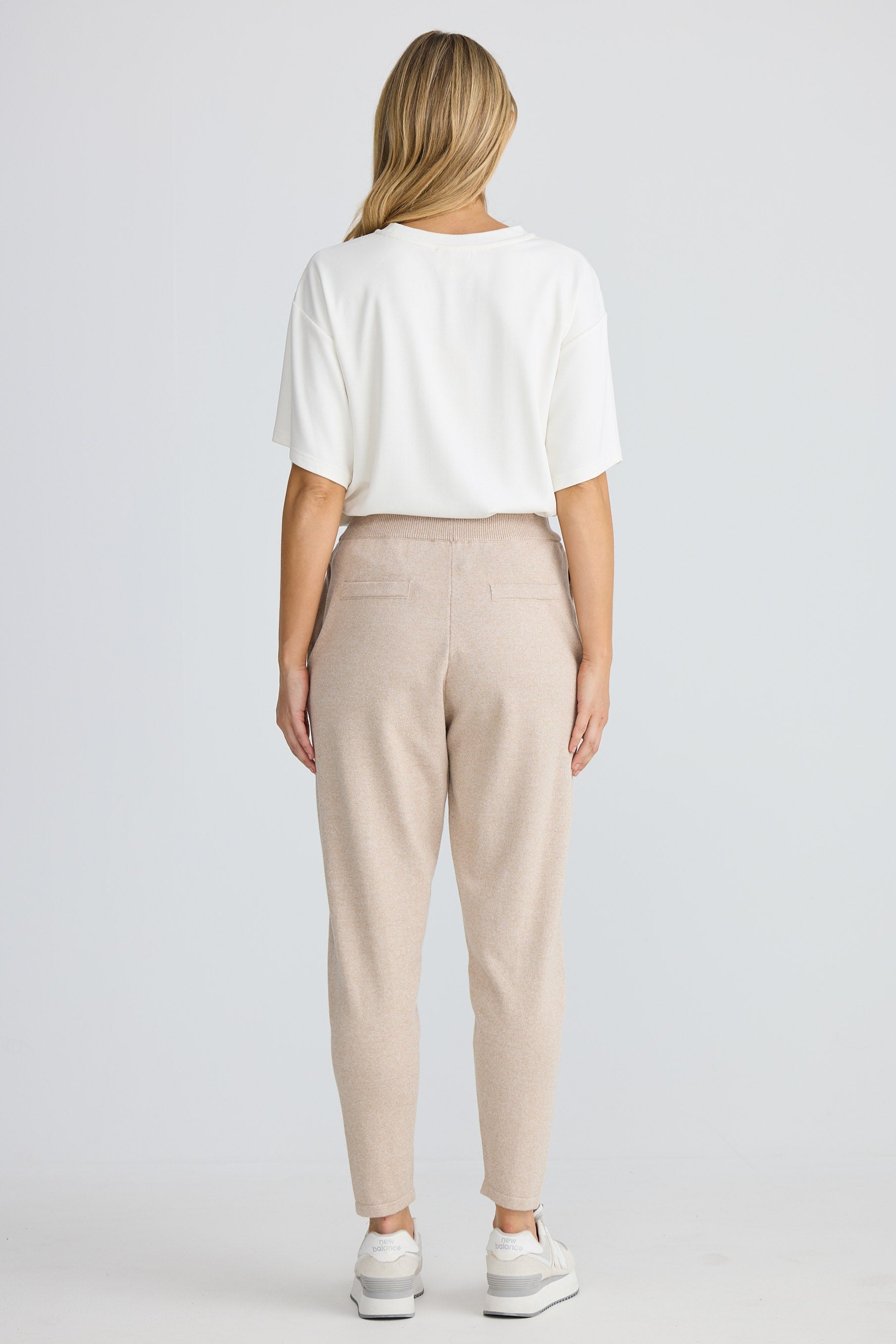 Person wearing a white top and beige pants on a plain background