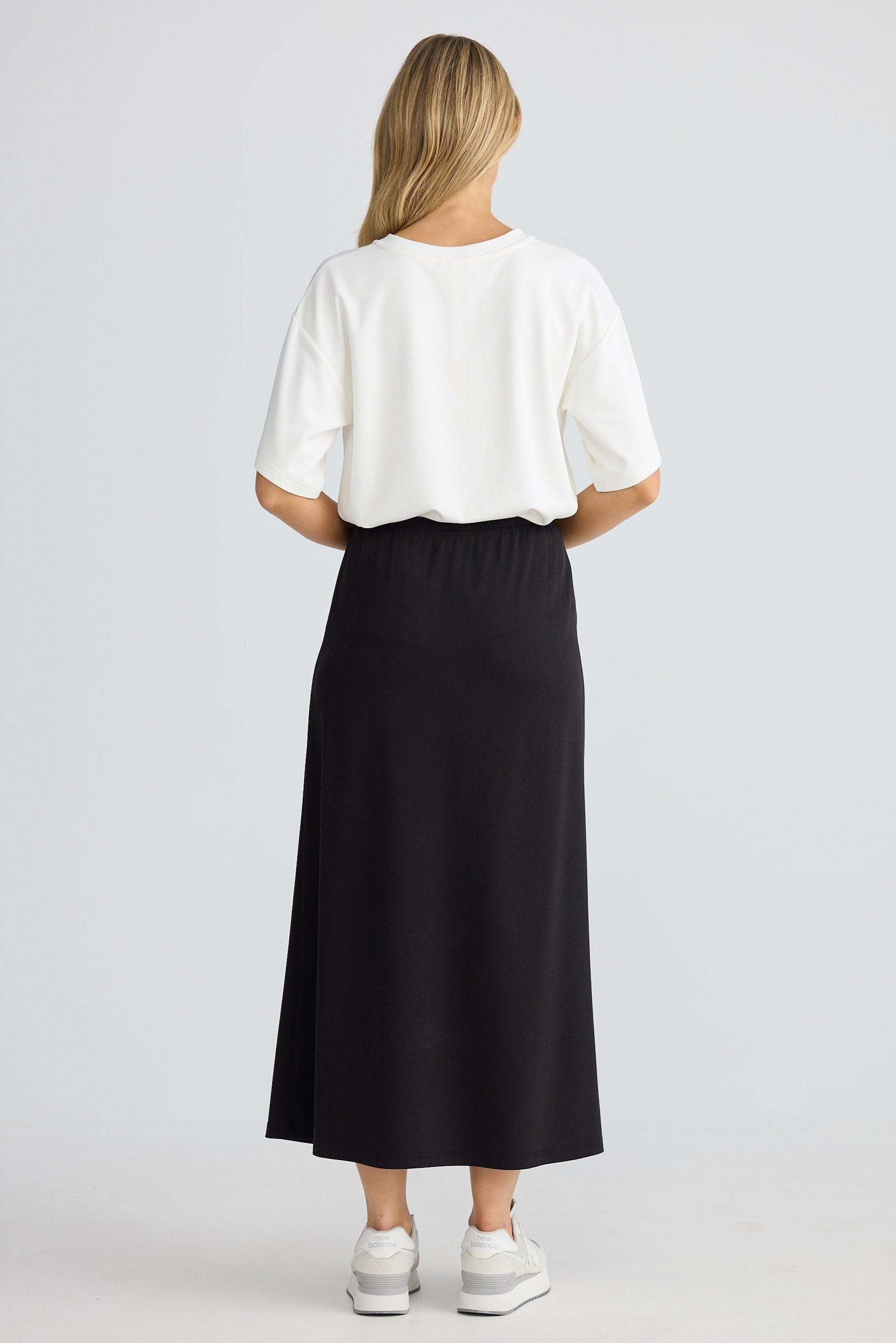 Person wearing a white top and black skirt on a light gray background