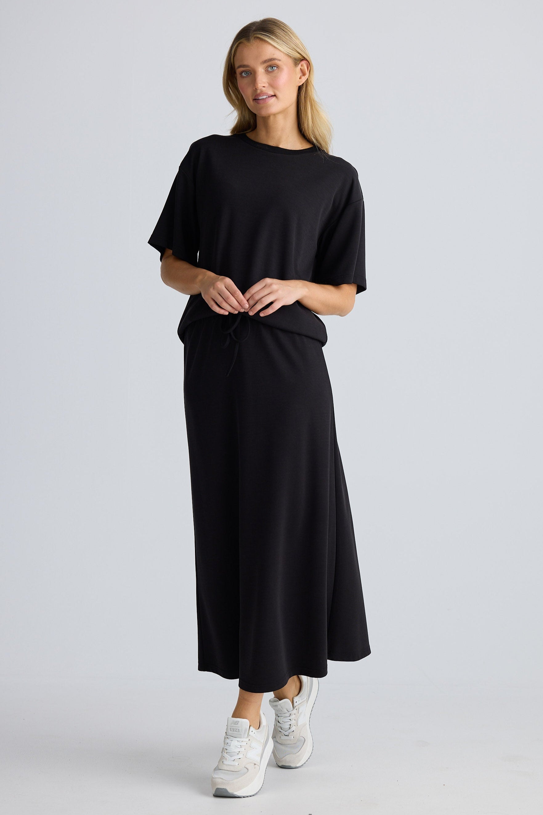 Woman wearing a black outfit with white sneakers on a light gray background