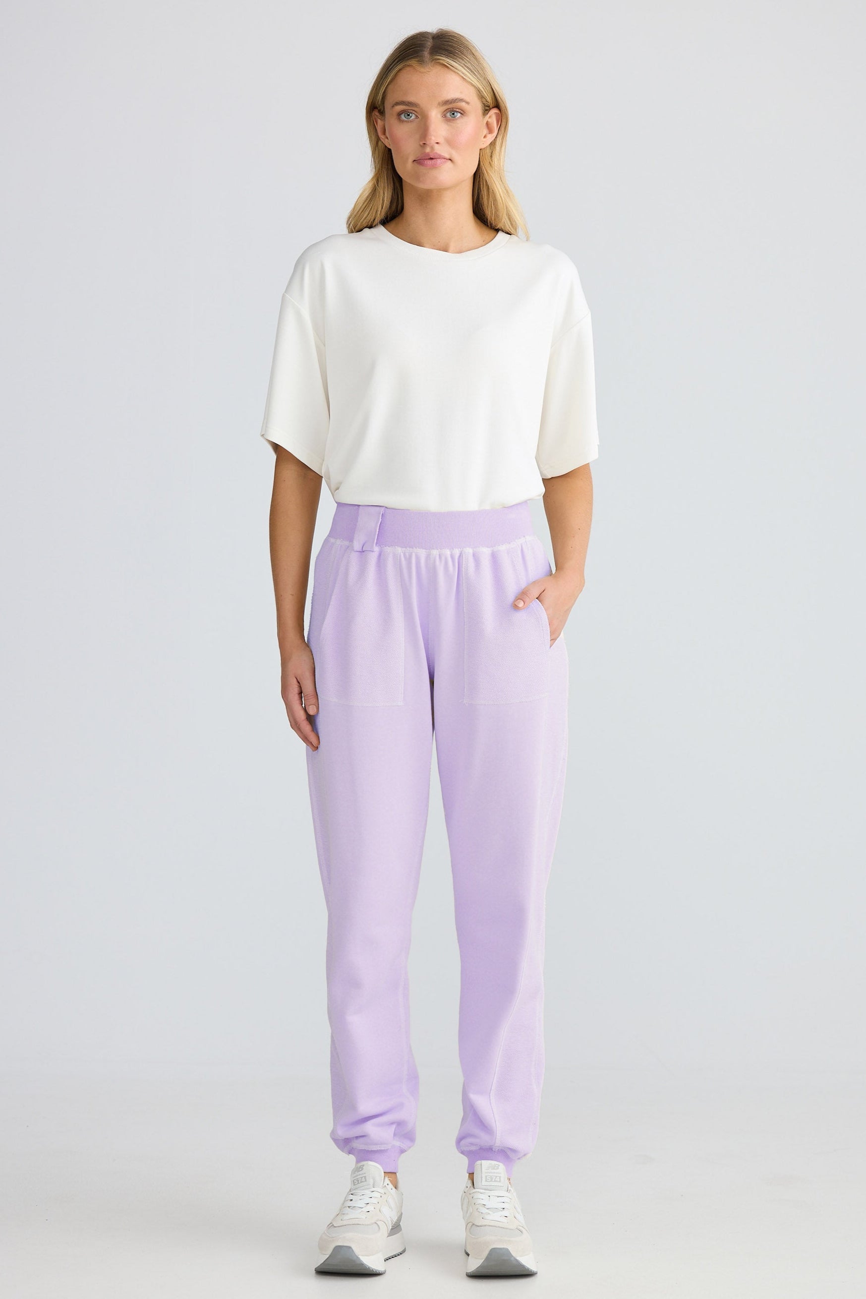Woman wearing a white top and lavender pants on a plain background
