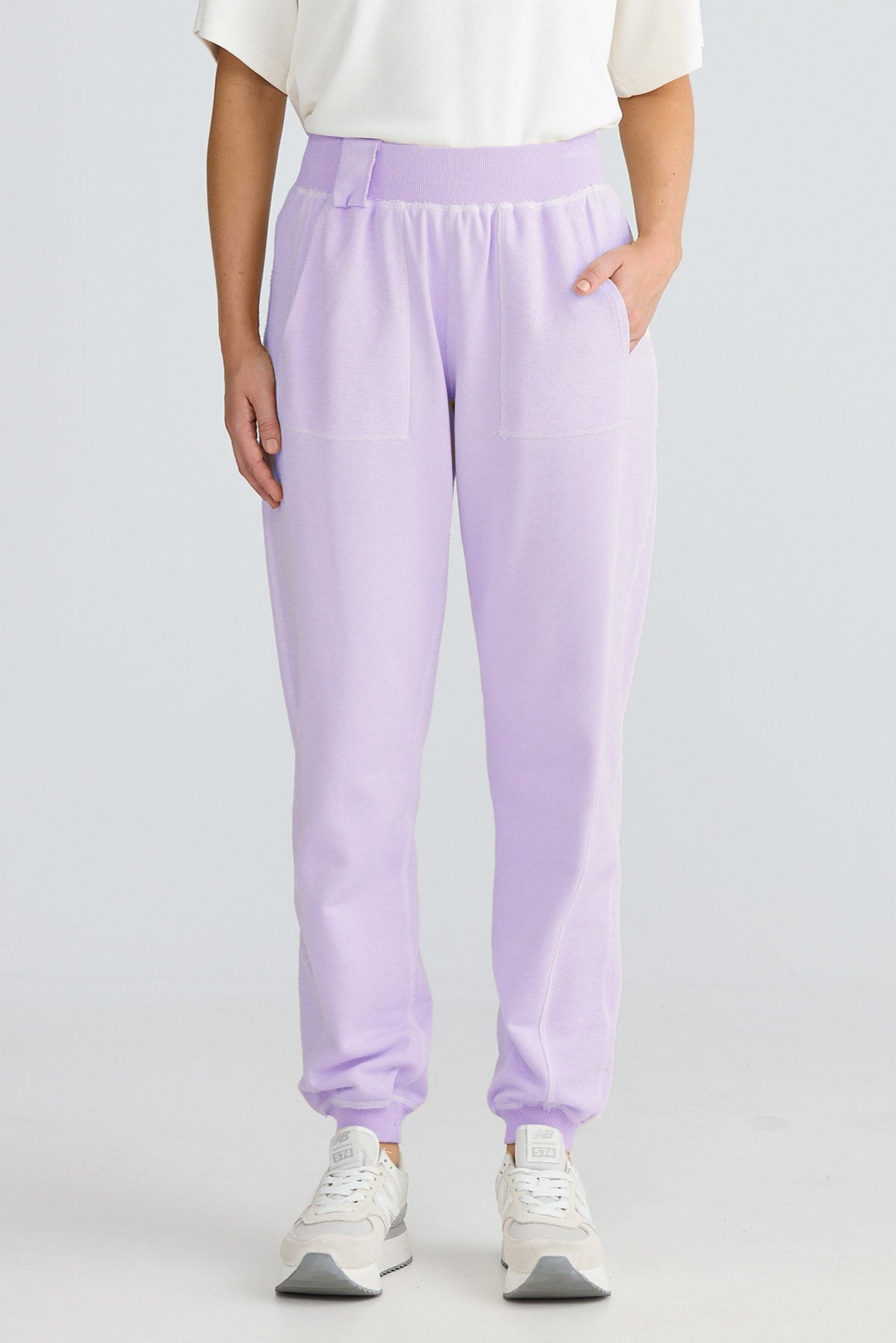 Woman wearing a white top and light purple pants on a plain background