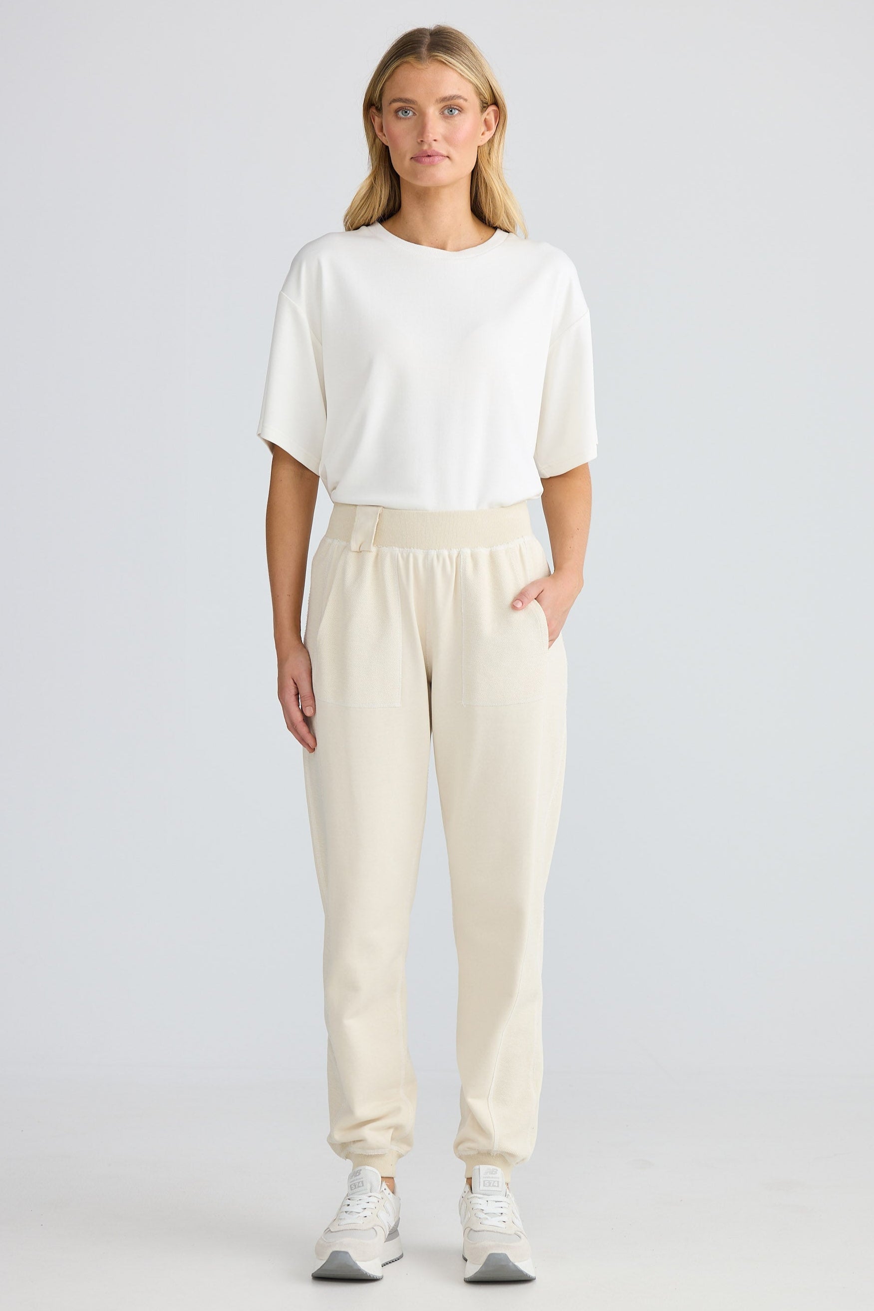 Woman wearing a white top and beige pants on a plain background