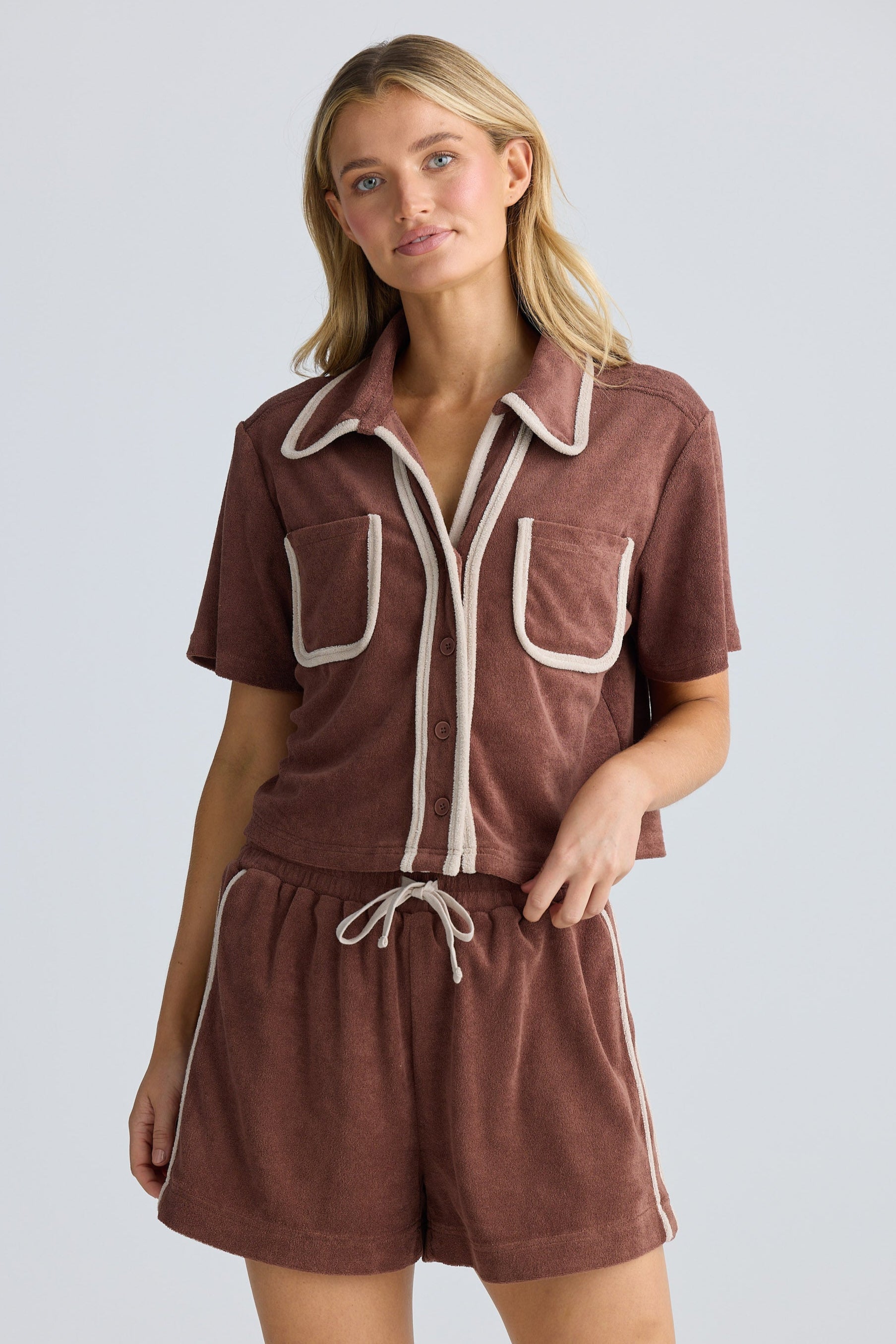 Woman wearing a brown outfit with white trim on a plain background