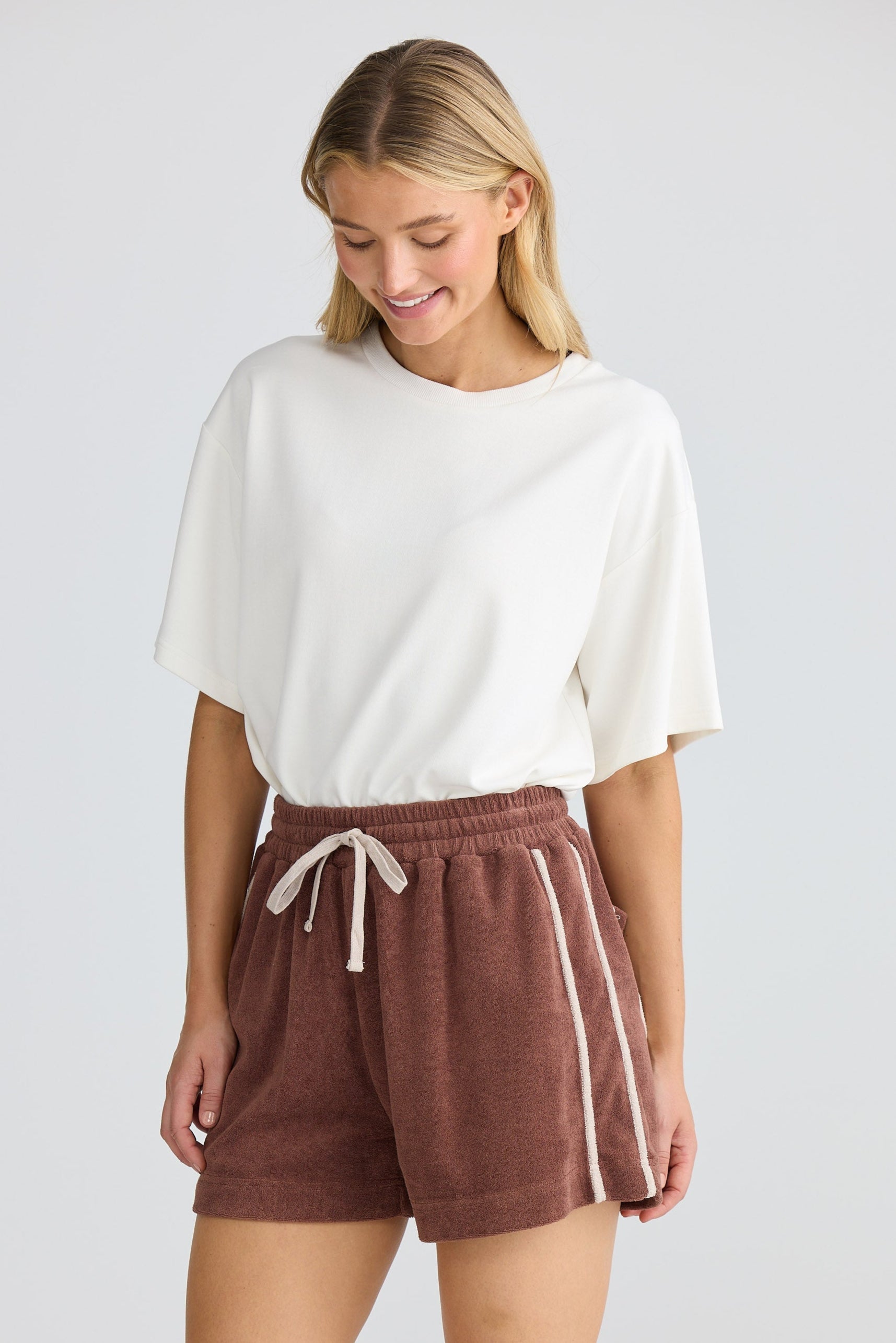 Woman wearing a white top and brown shorts with a white background