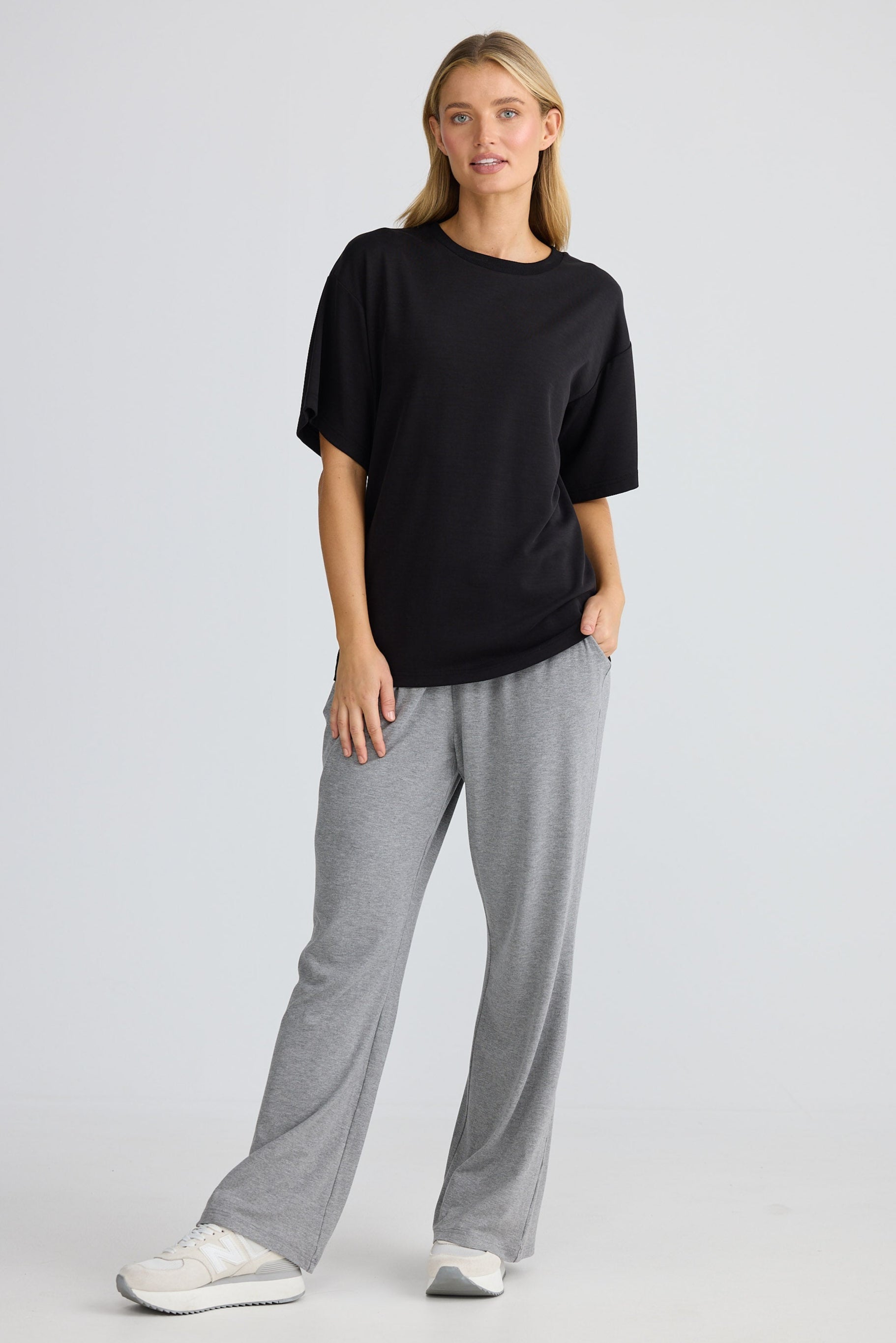 Woman wearing a black oversized t-shirt and gray pants on a white background