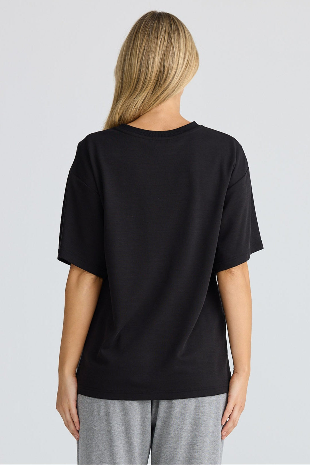 Person wearing a black t-shirt and gray pants on a white background