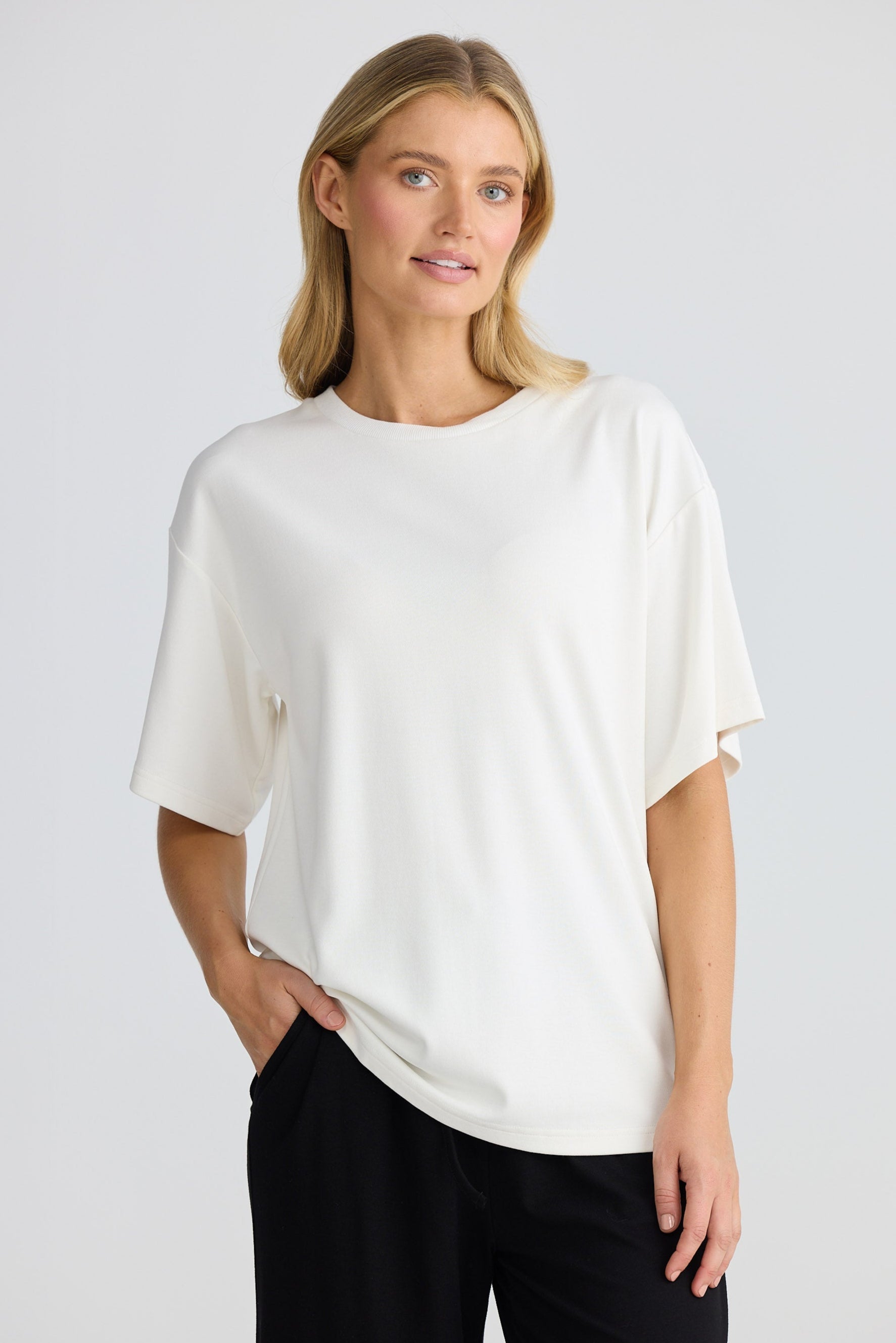 Woman wearing a white t-shirt and black pants on a plain background