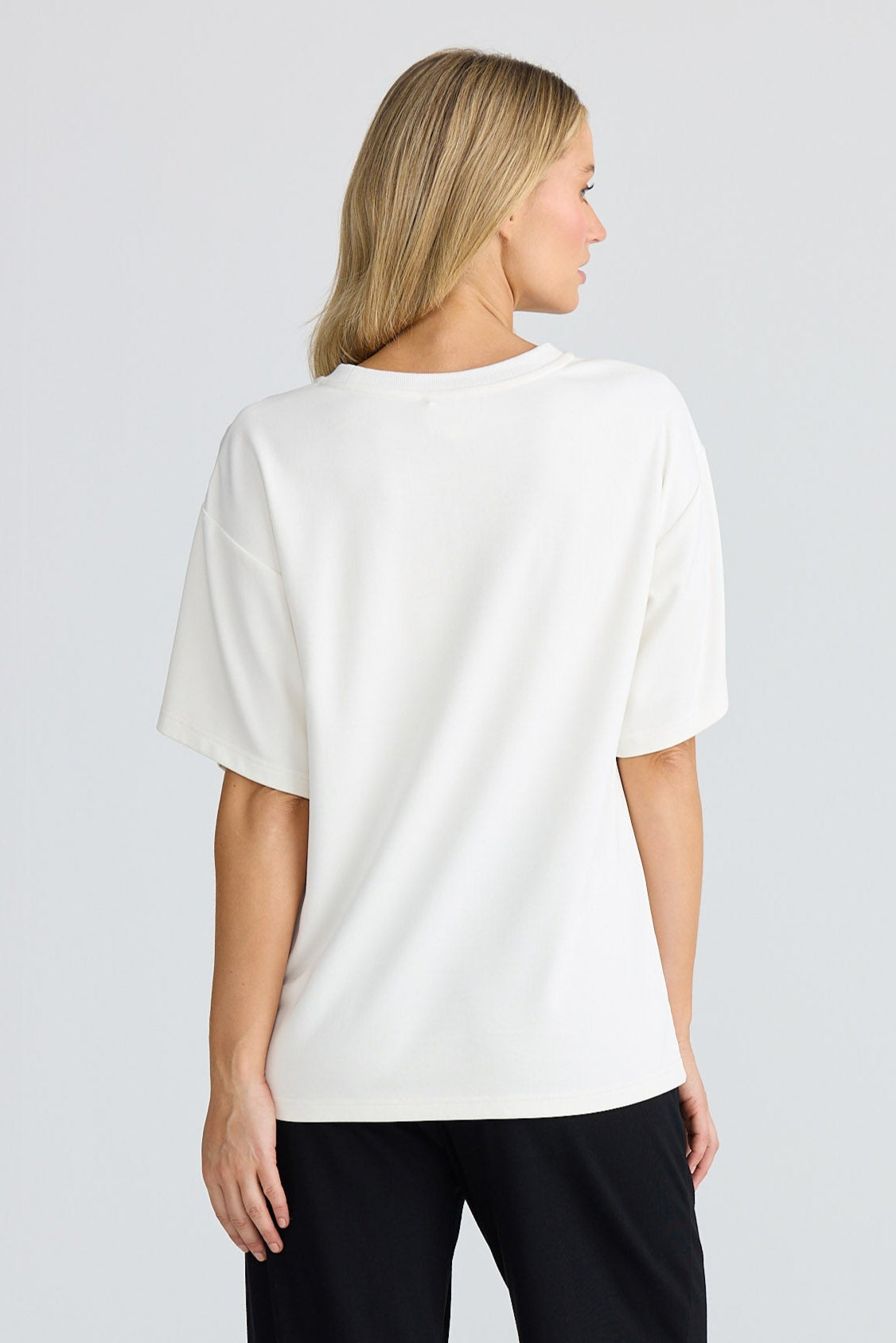 Woman wearing a white oversized shirt and black pants on a plain background