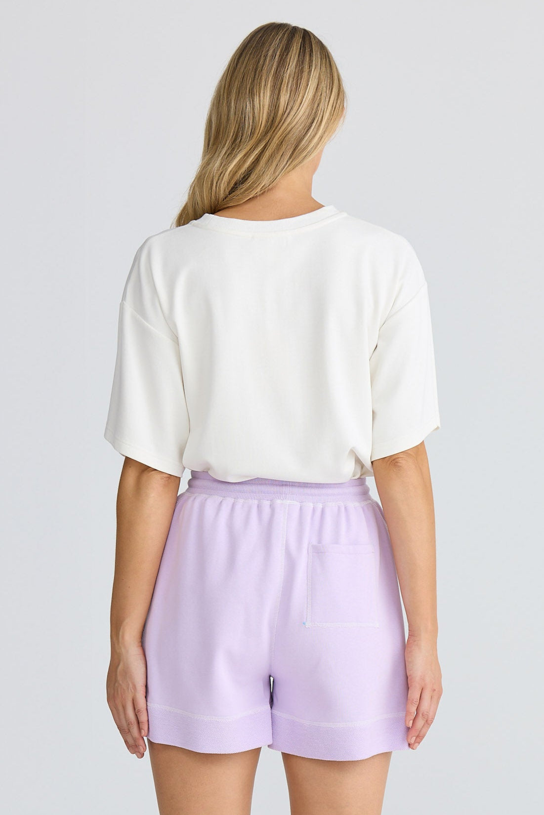 Person wearing a white top and lavender shorts on a plain background