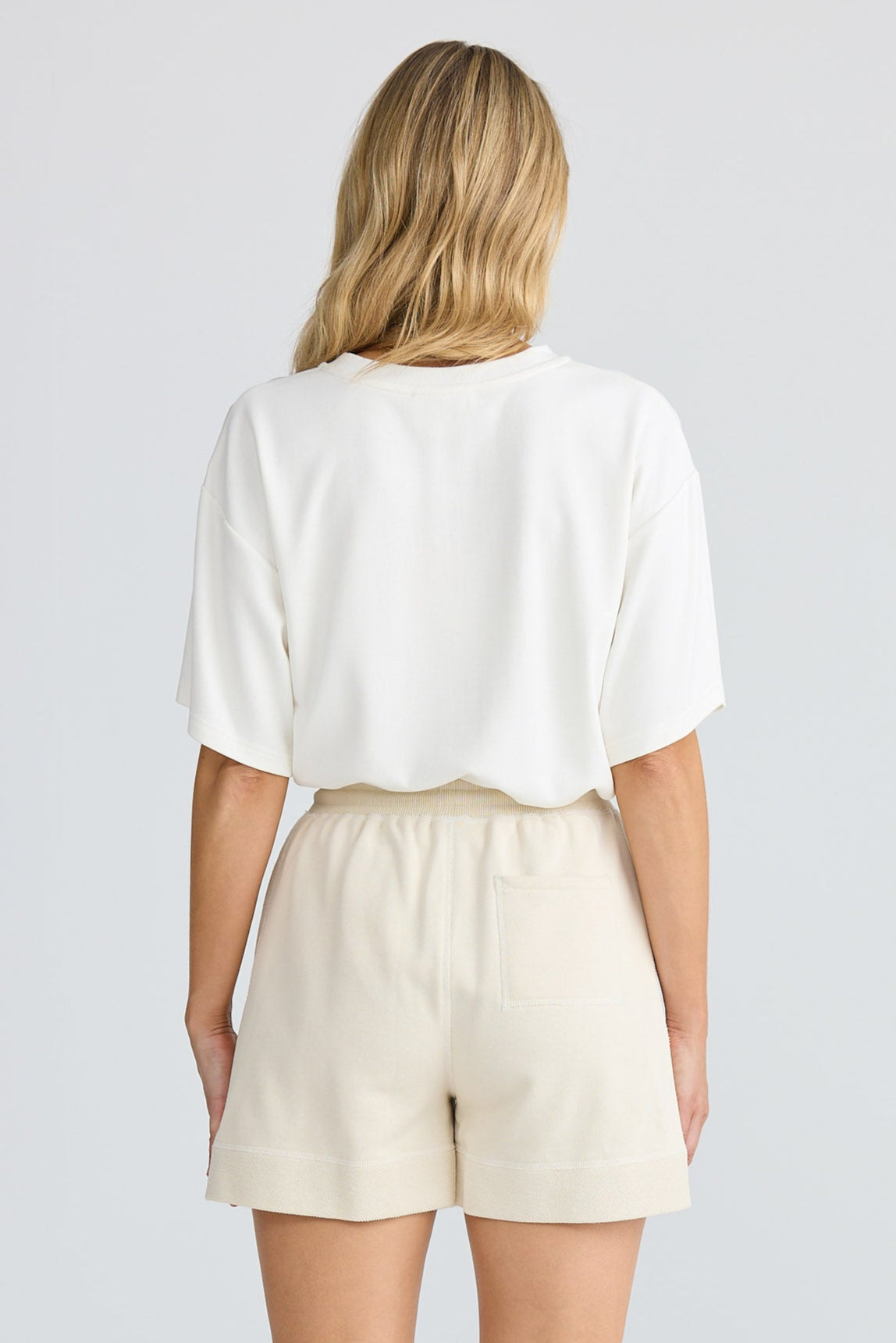 Person wearing a white top and beige shorts on a plain background