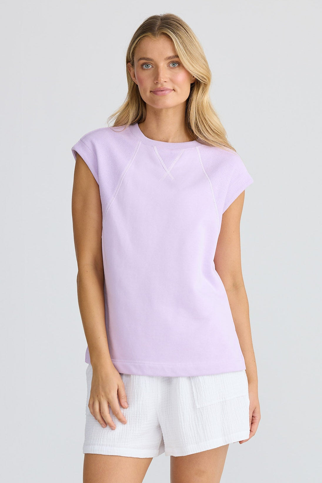 Woman wearing a light purple sleeveless top and white shorts on a white background