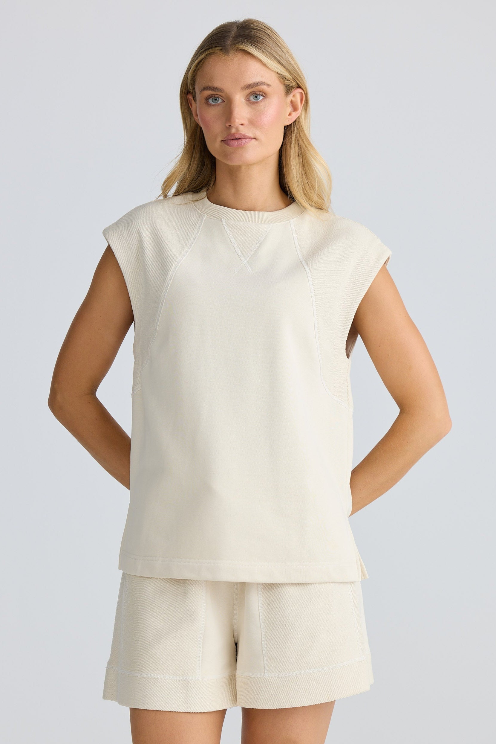 Woman wearing a cream-colored sleeveless top and shorts on a light gray background