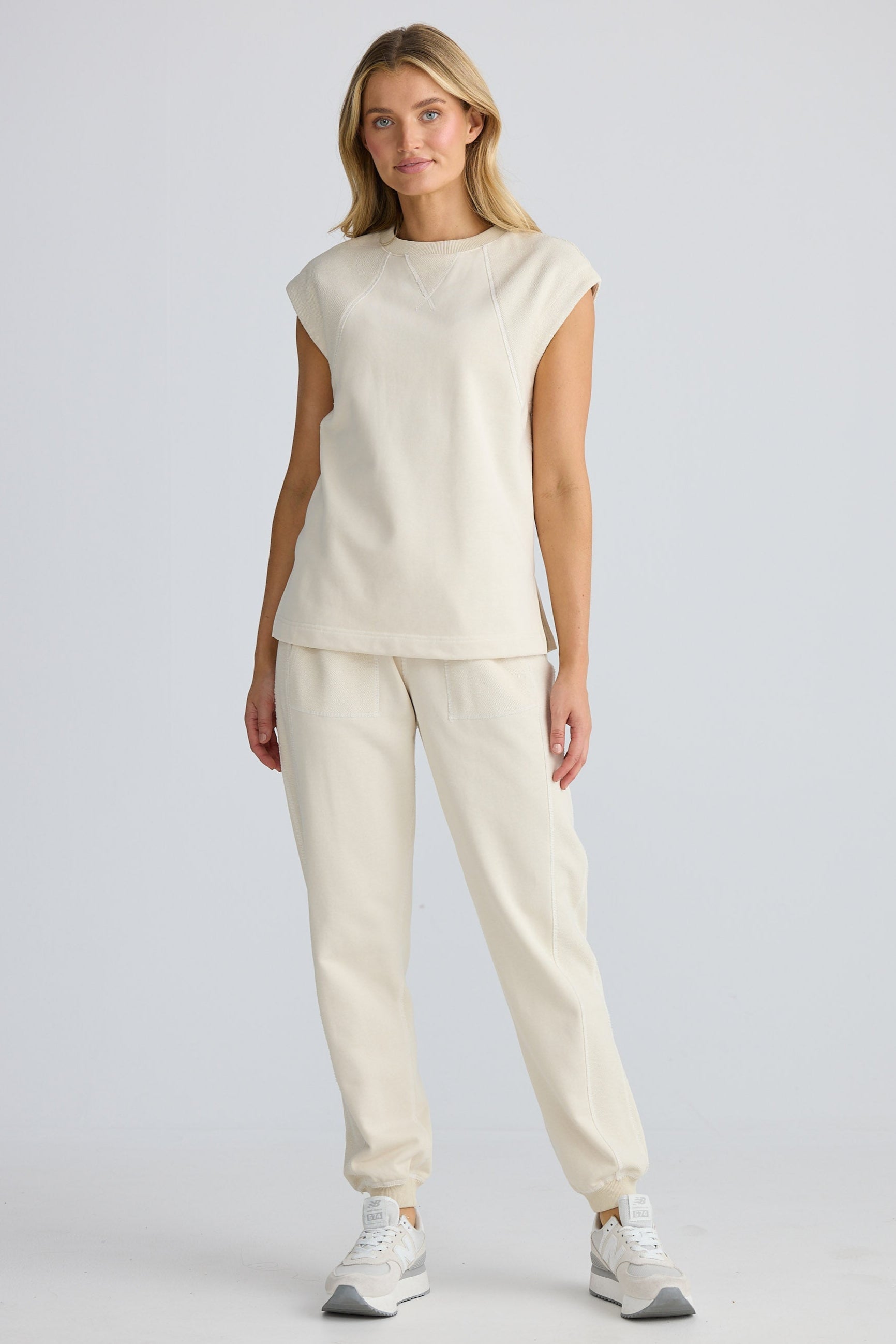 Woman wearing a beige sleeveless top and pants on a white background
