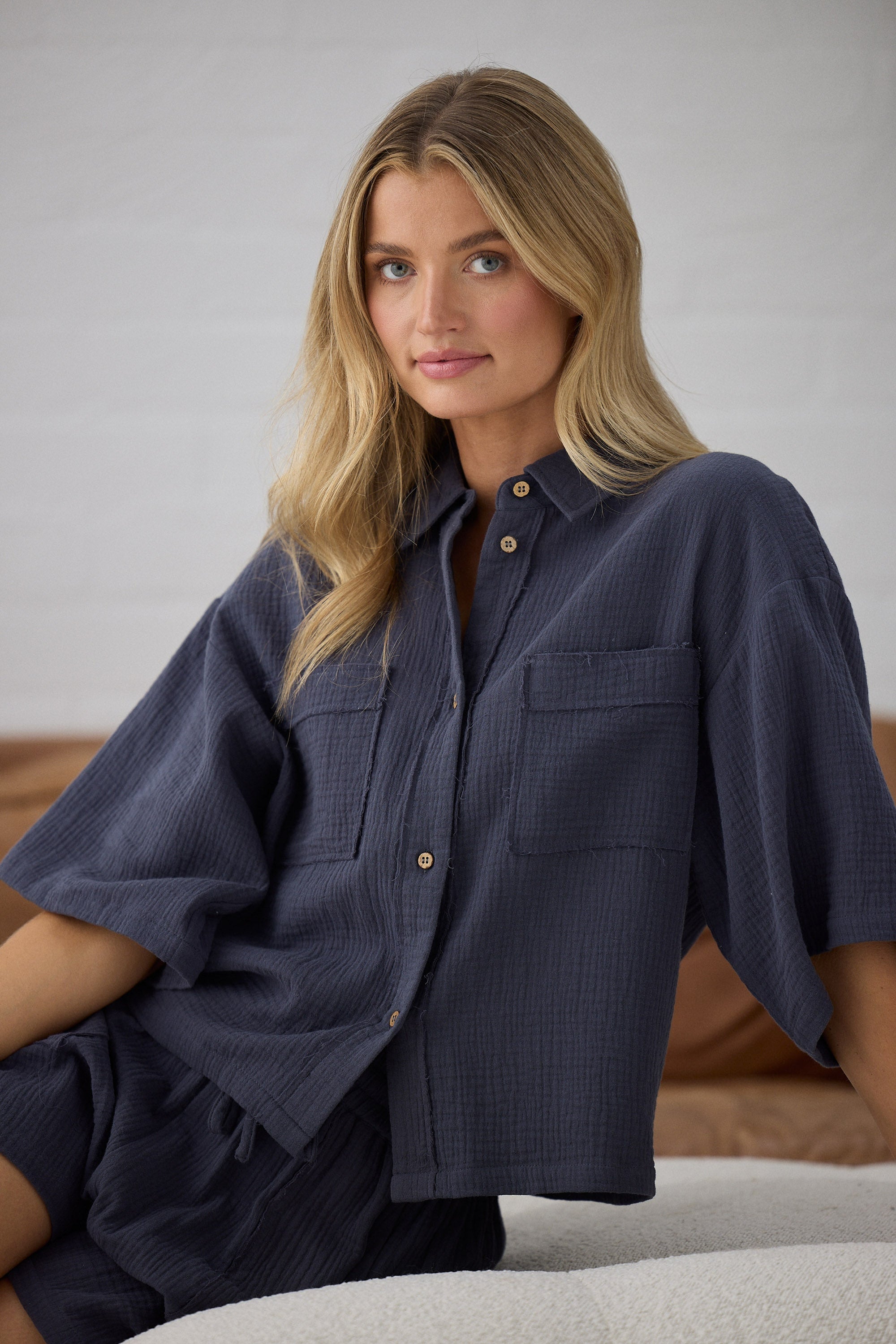 Woman wearing a navy blue outfit sitting on a couch against a neutral background