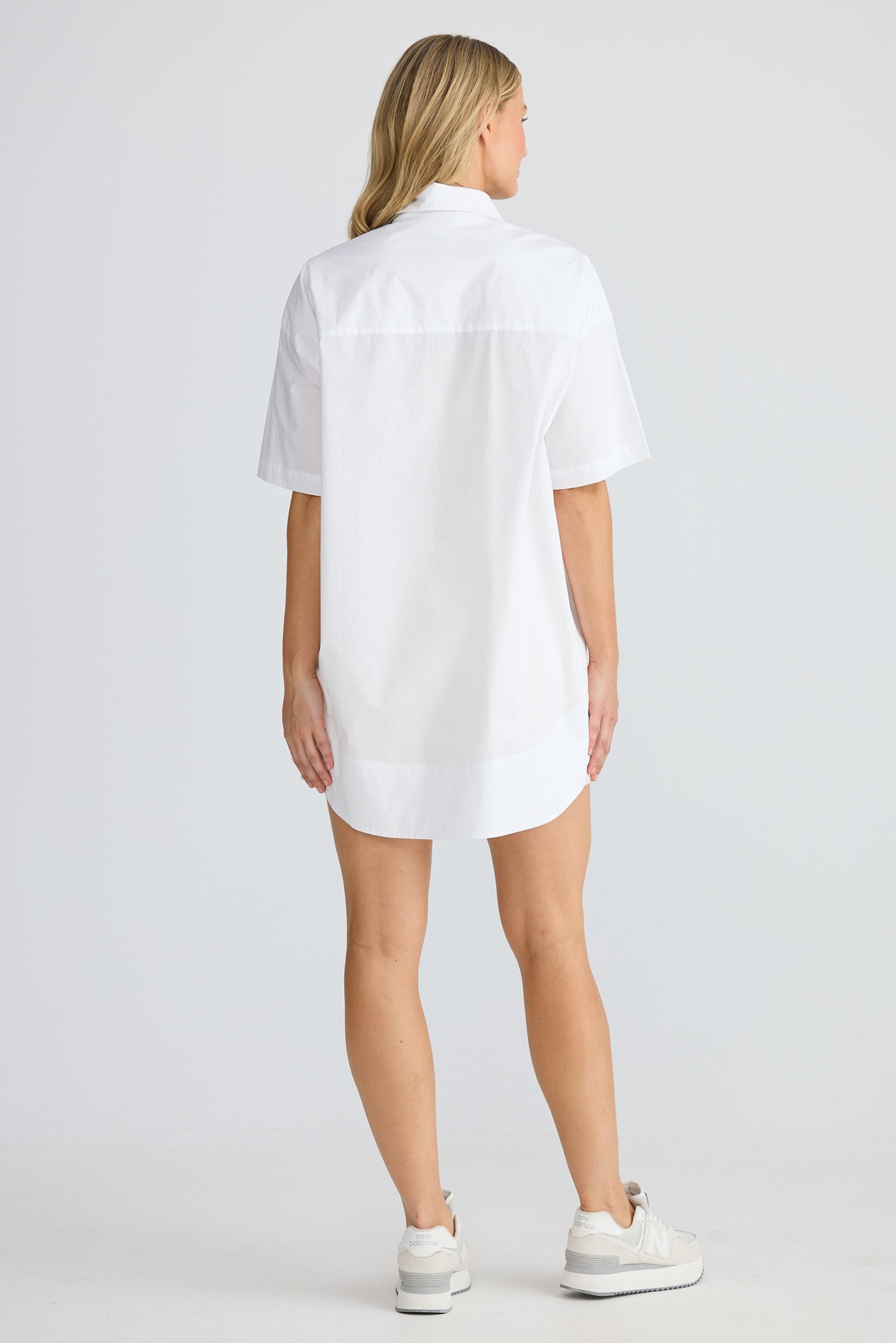 Woman wearing a white shirt dress on a plain background