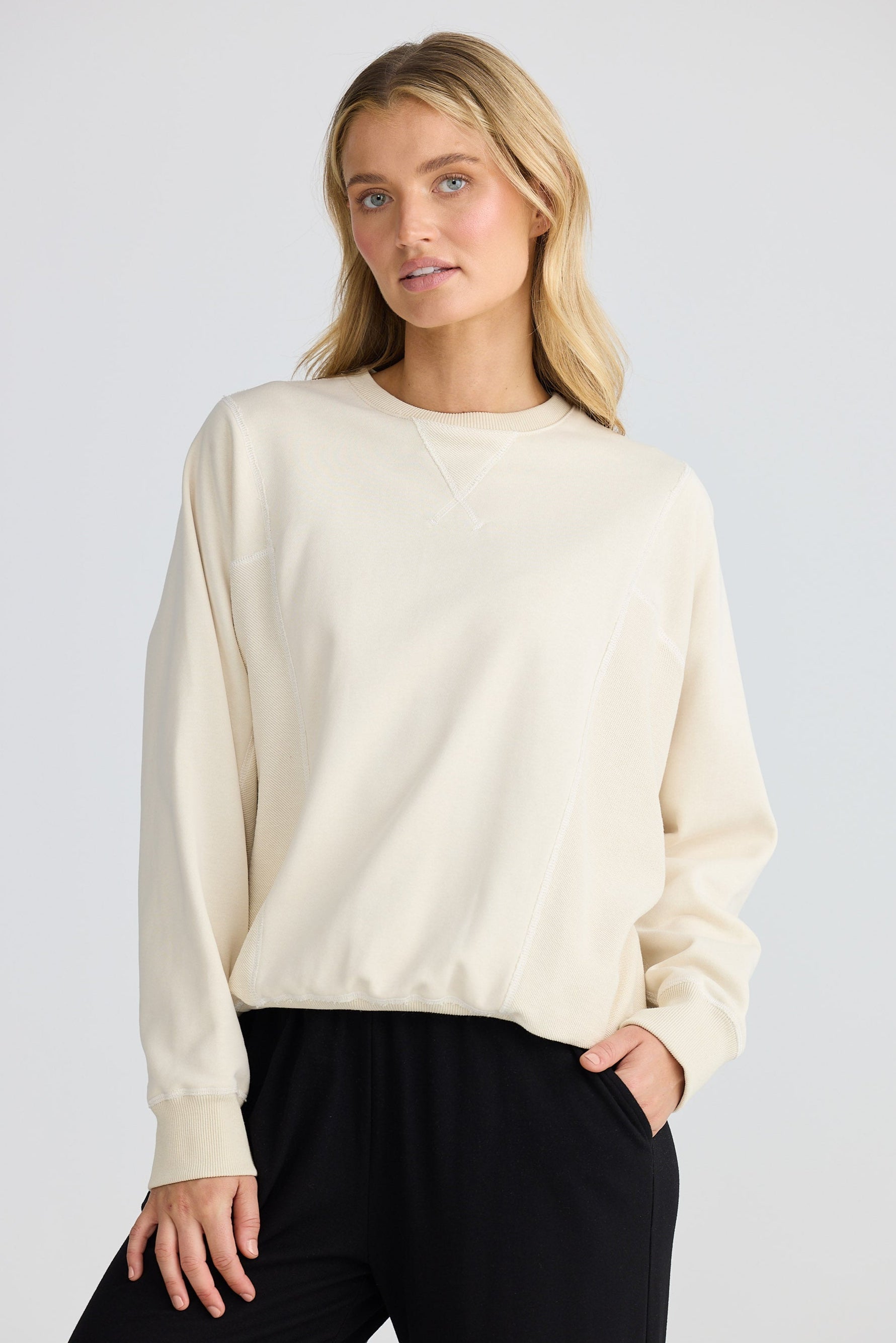 Woman wearing a cream sweater and black pants on a white background