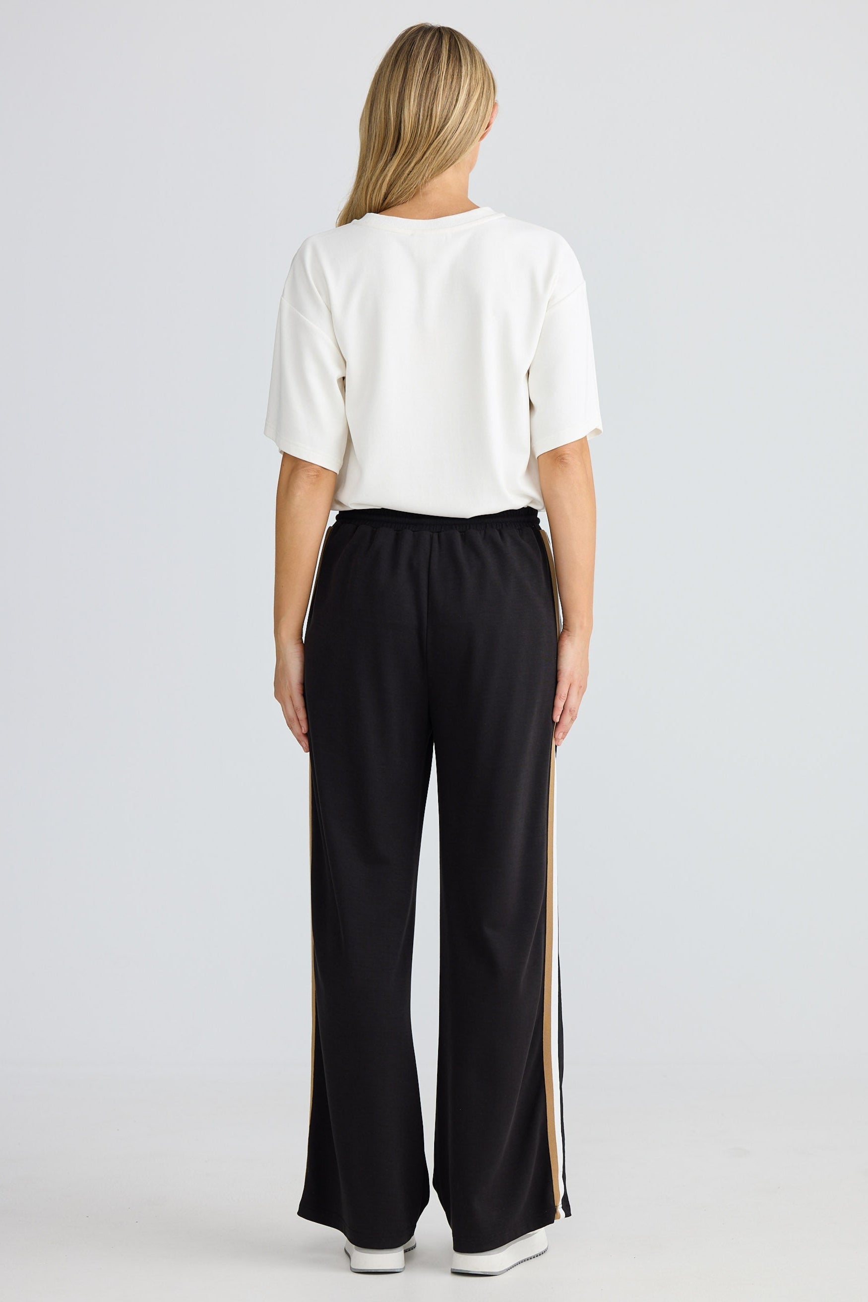 Person wearing a white top and black pants with a stripe on a white background