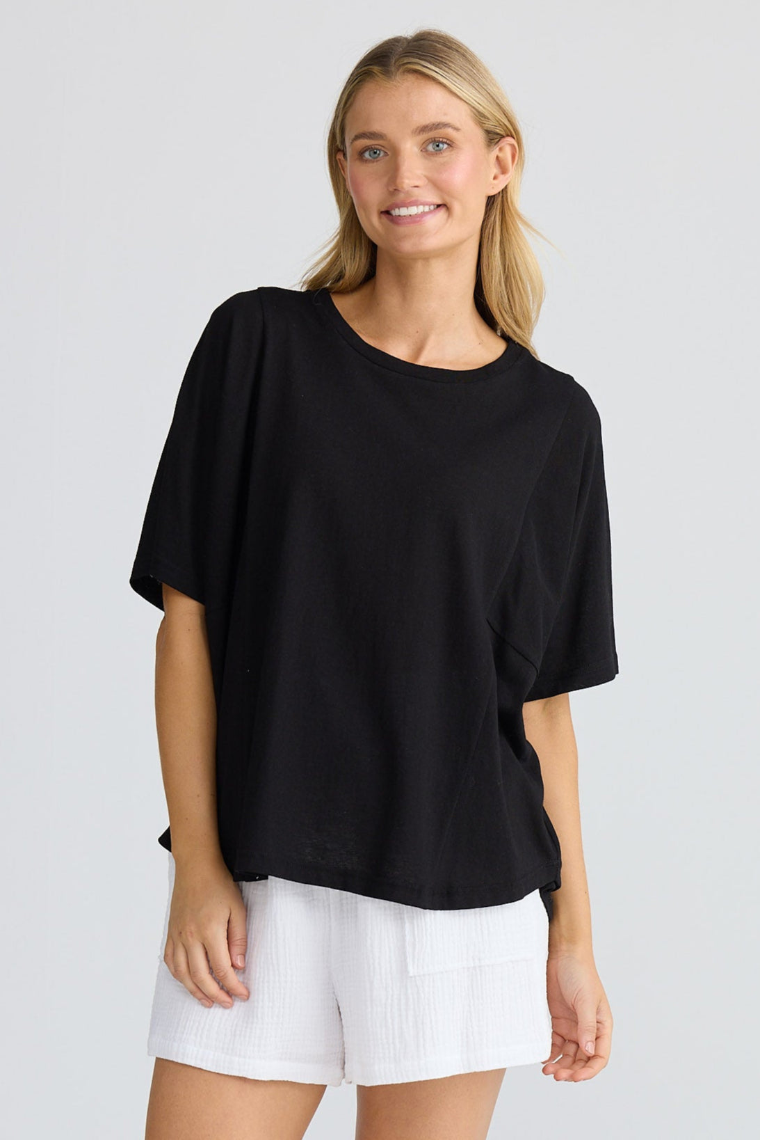 Woman wearing a black top and white shorts on a light gray background