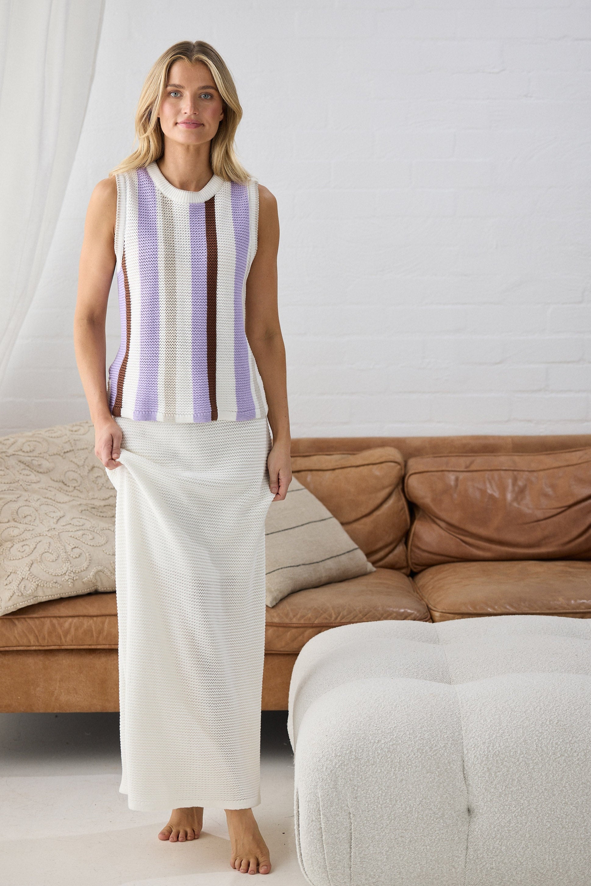 Woman wearing a striped sleeveless top and white pants in a living room.