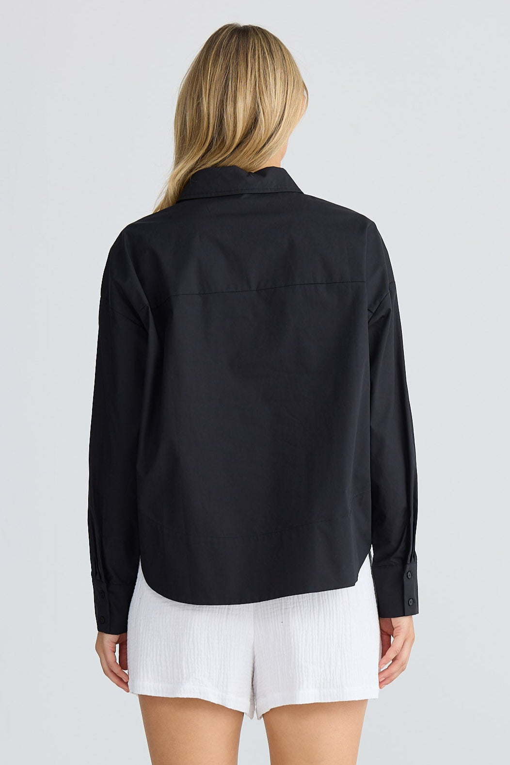 Person wearing a black long-sleeve shirt and white shorts on a plain background