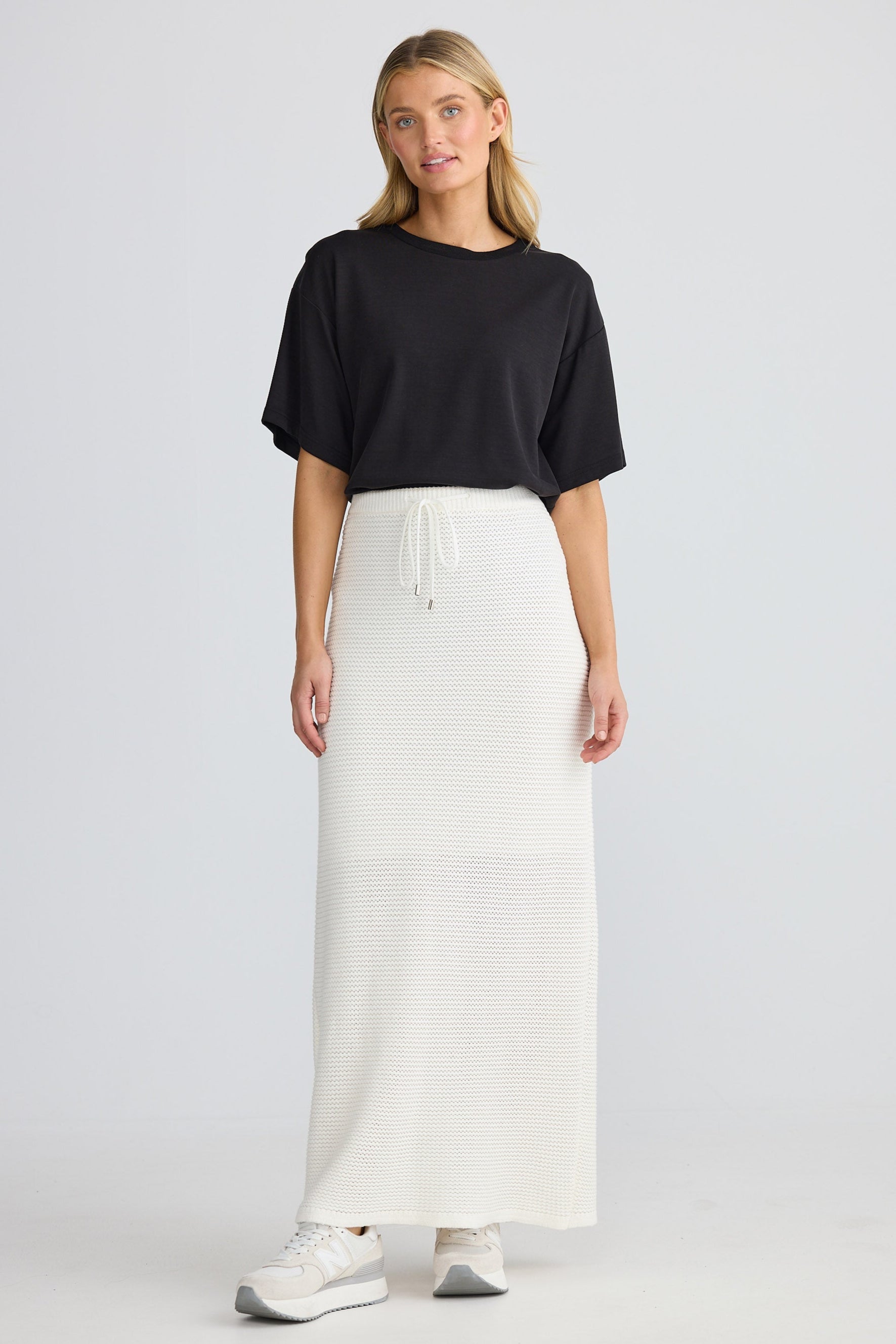 Woman wearing a black top and white skirt on a light gray background