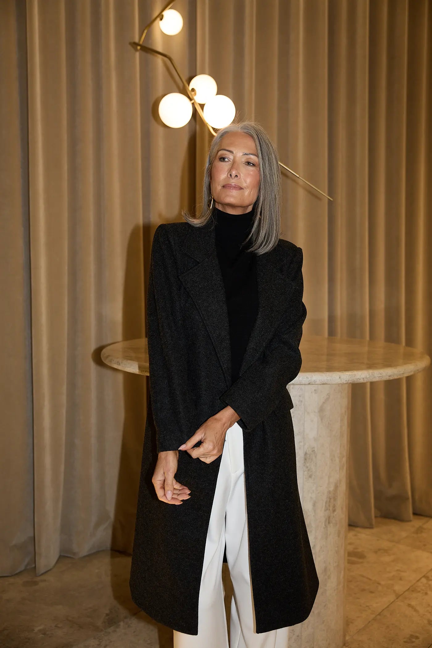 Model wearing a charcoal longline coat layered over a black knit and white trousers for a refined autumn look in modern Australian women’s fashion.