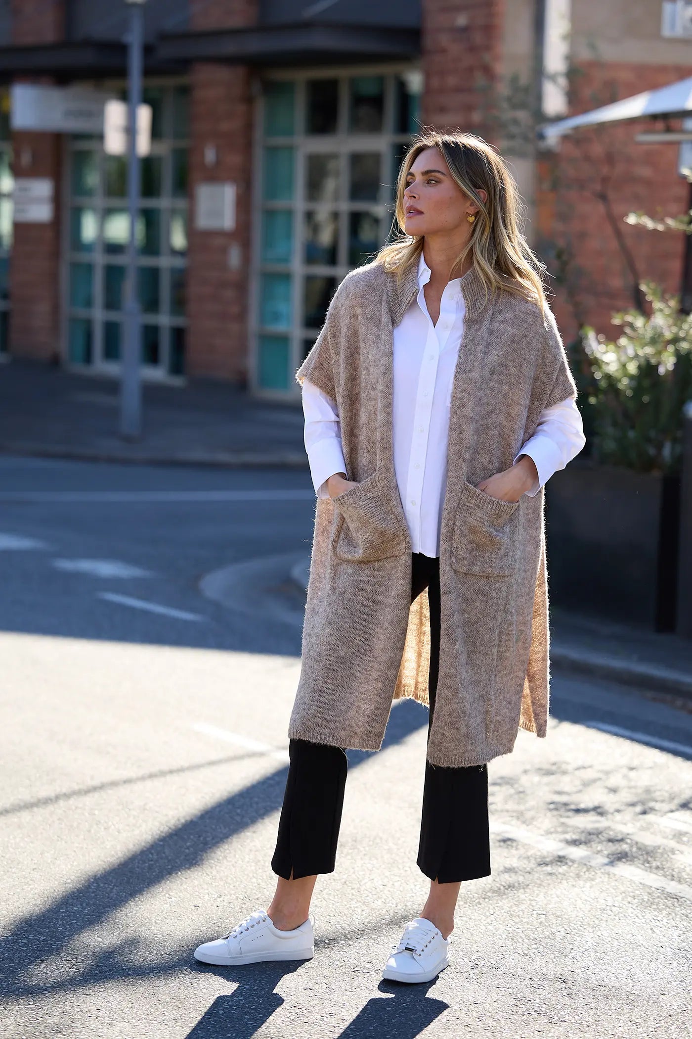 Model wearing an oat marle longline knit cardigan with patch pockets, layered over a white shirt and black trousers for an effortless autumn look.