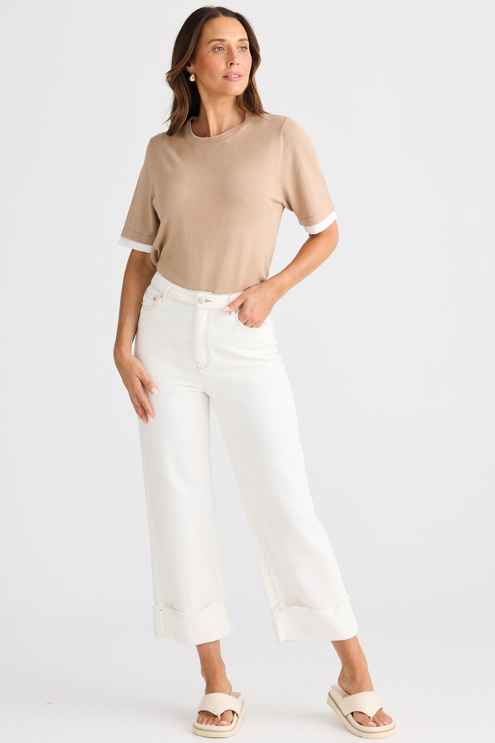 Woman wearing a beige top and white pants on a white background