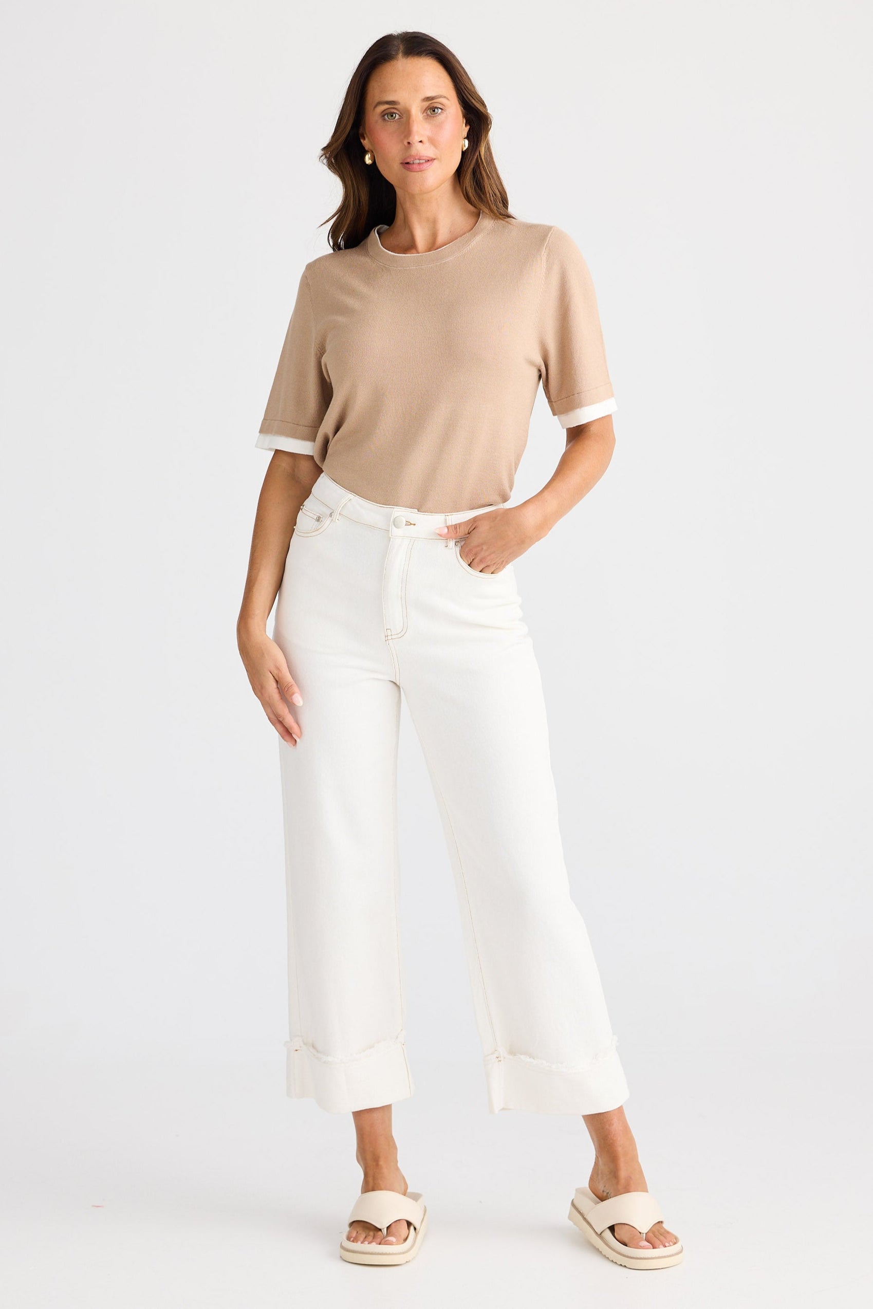 Woman wearing a beige top and white pants on a white background