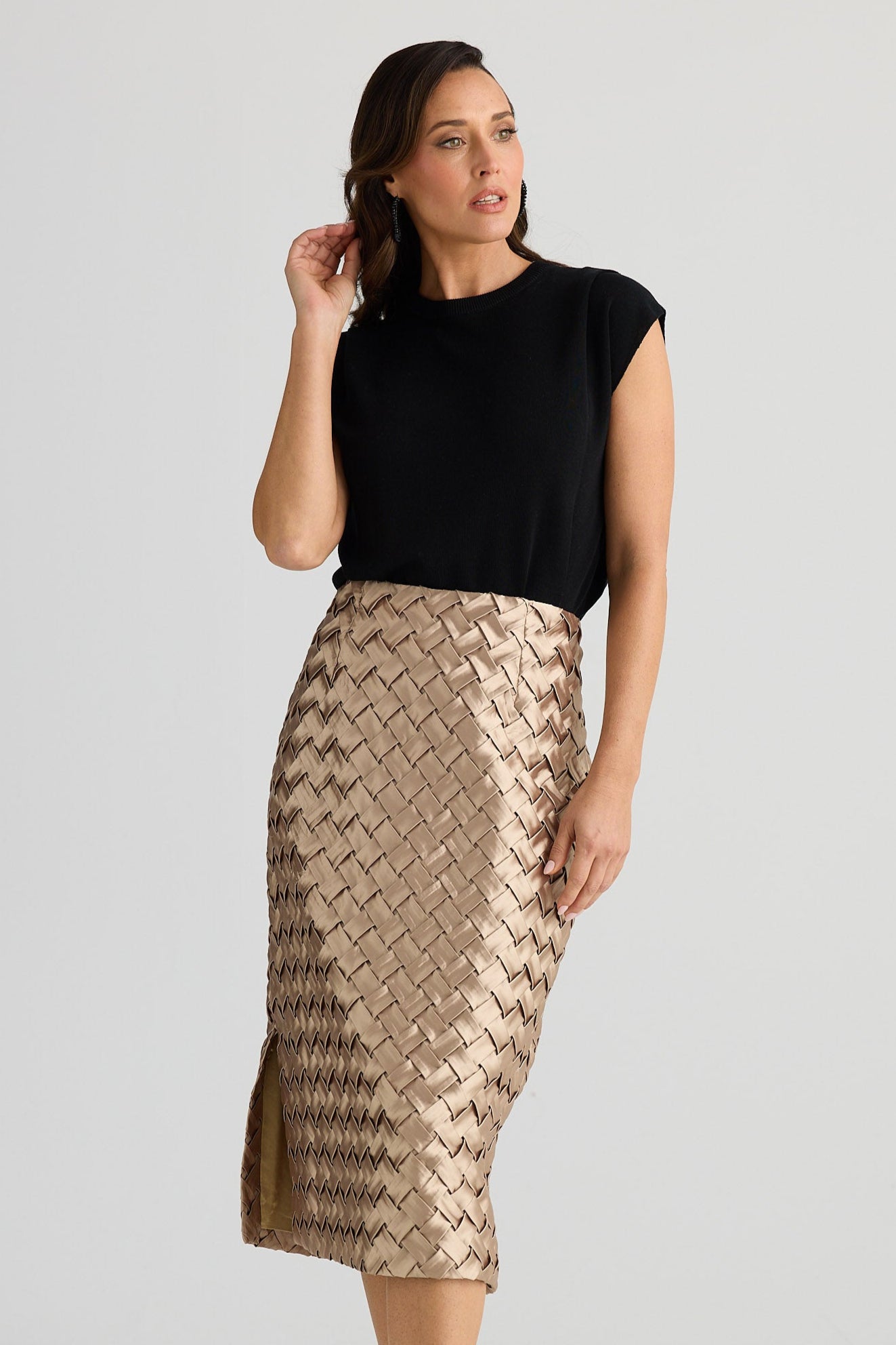 Woman wearing a black top and gold patterned skirt on a white background
