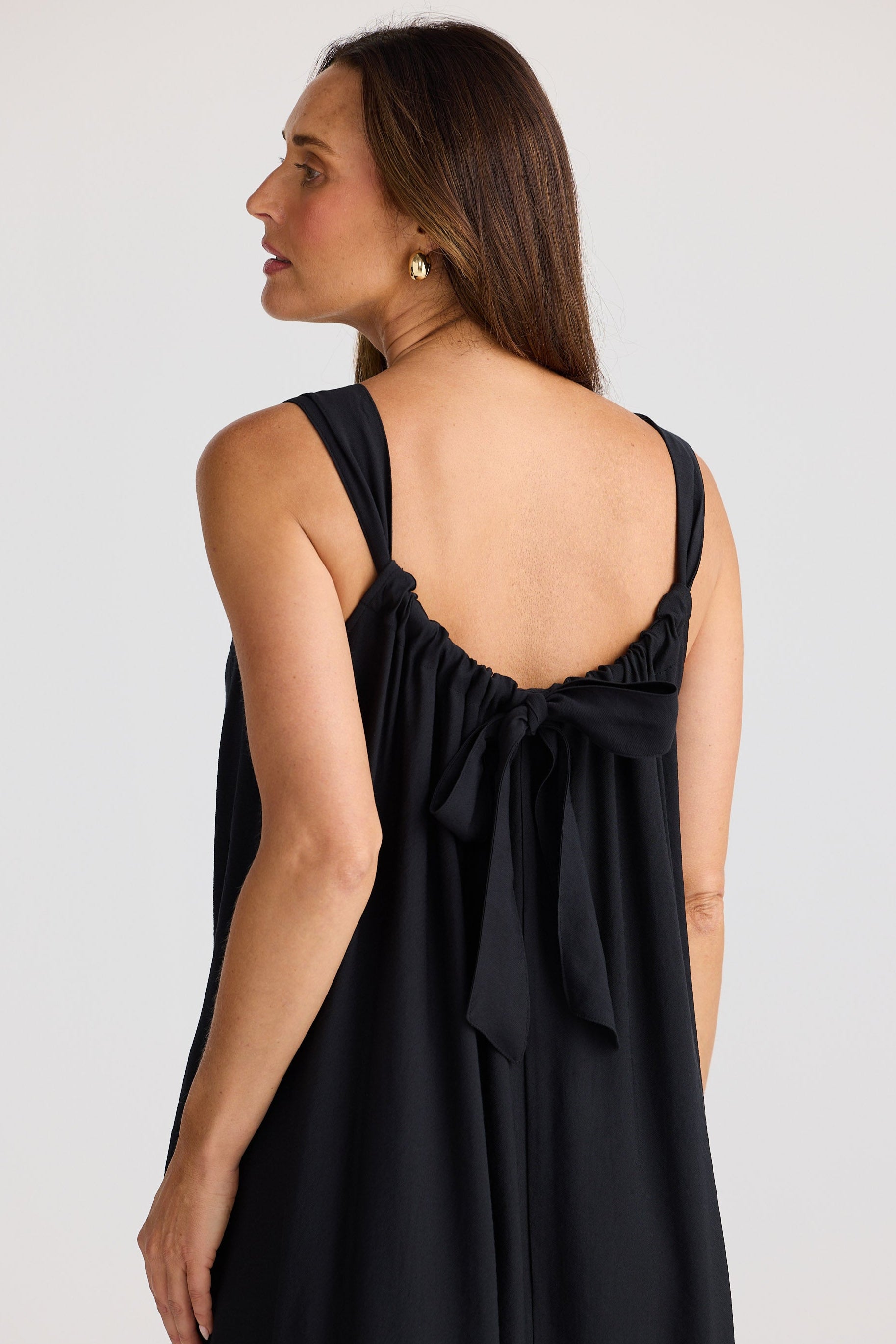 Woman wearing a black sleeveless dress with a bow detail on a white background