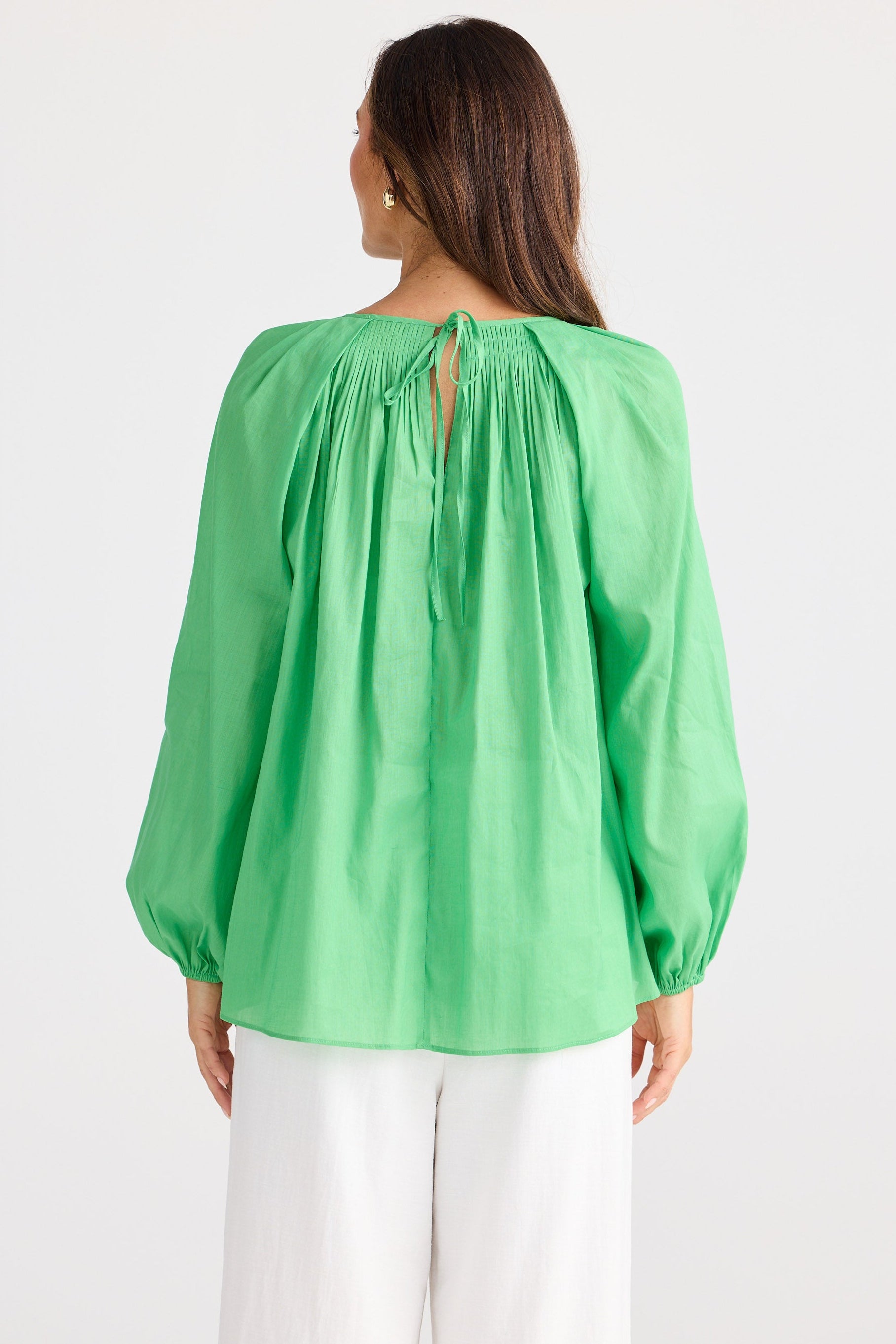 Woman wearing a green blouse with long sleeves and a keyhole neckline on a white background