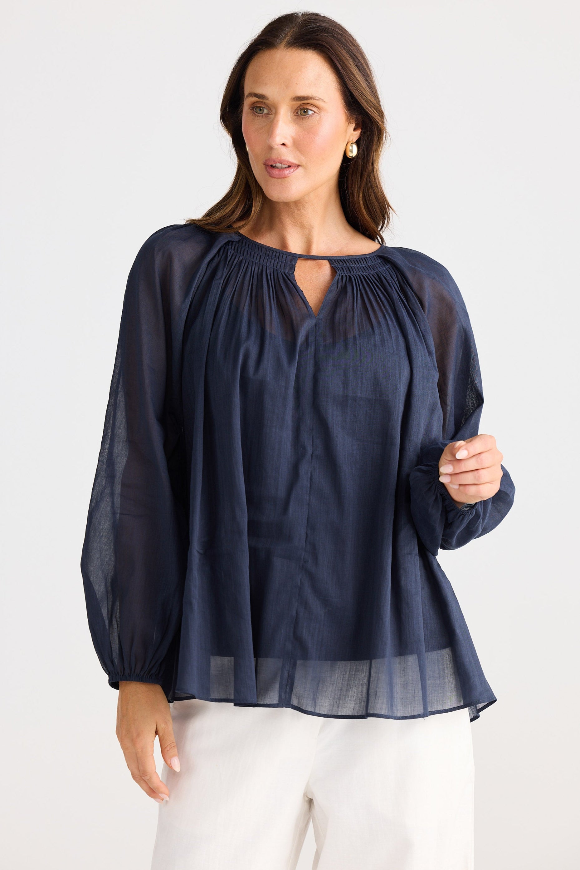 Woman wearing a navy blue blouse with sheer sleeves on a white background