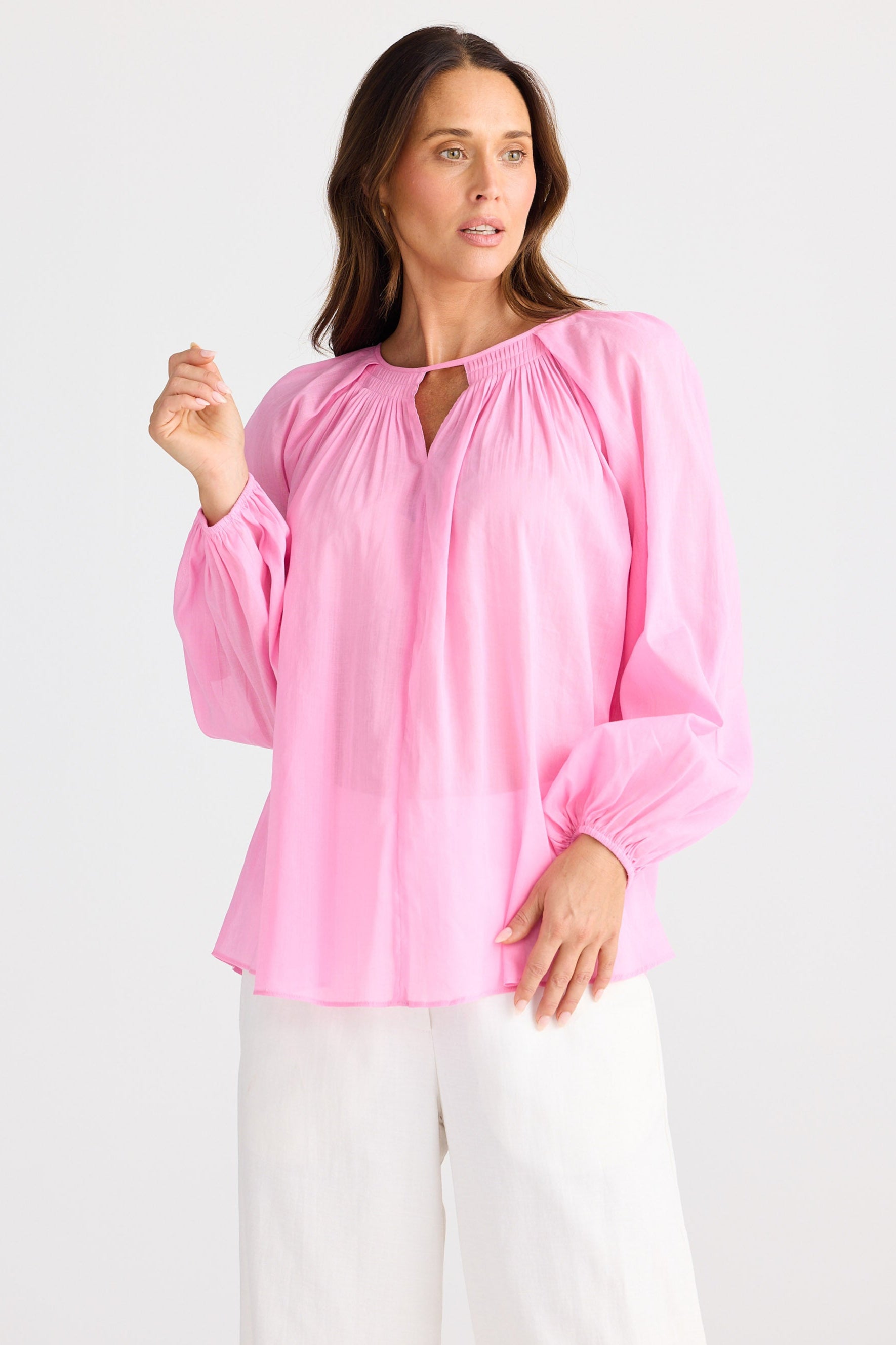 Woman wearing a pink blouse and white pants on a light gray background