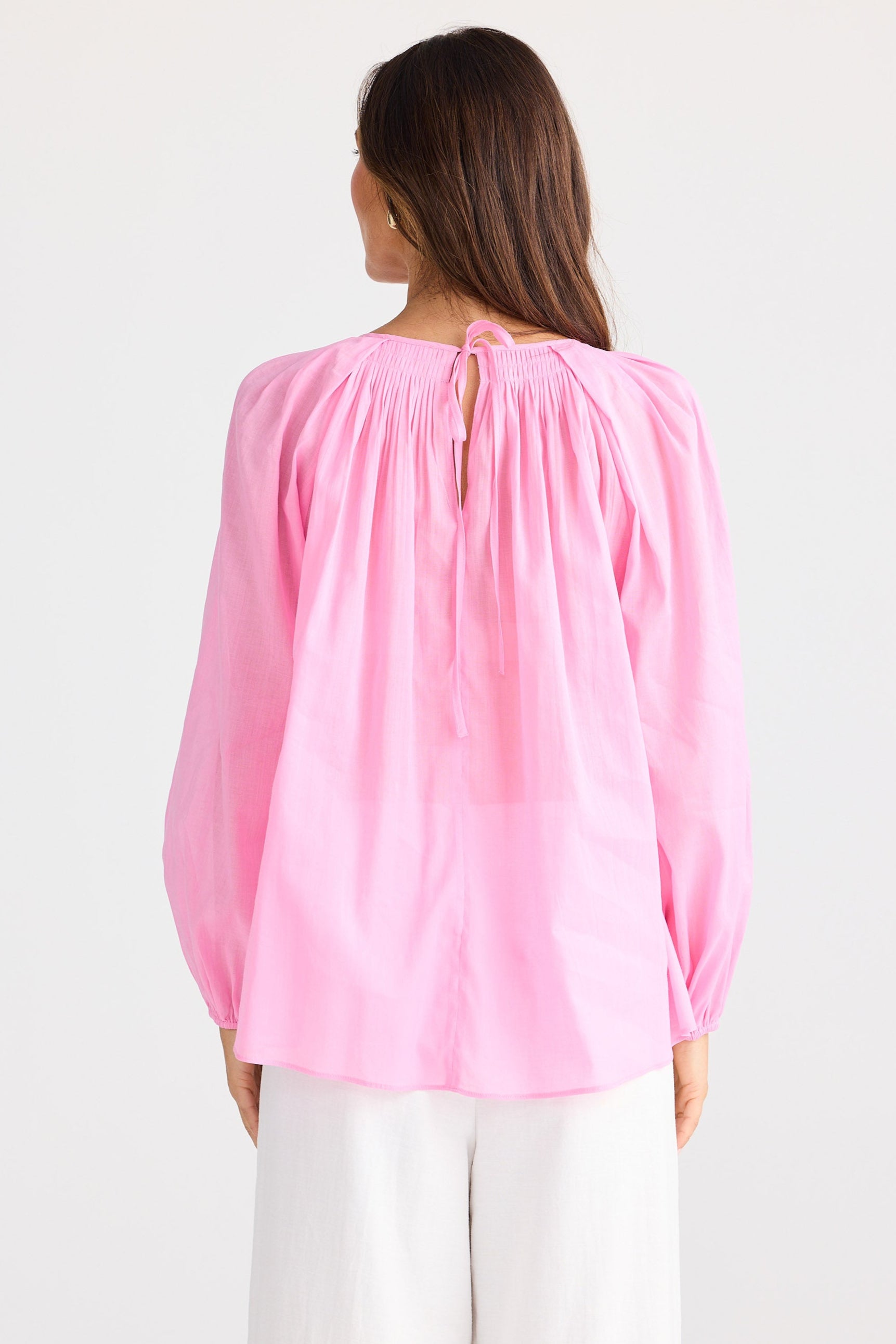 Woman wearing a pink blouse with long sleeves on a white background