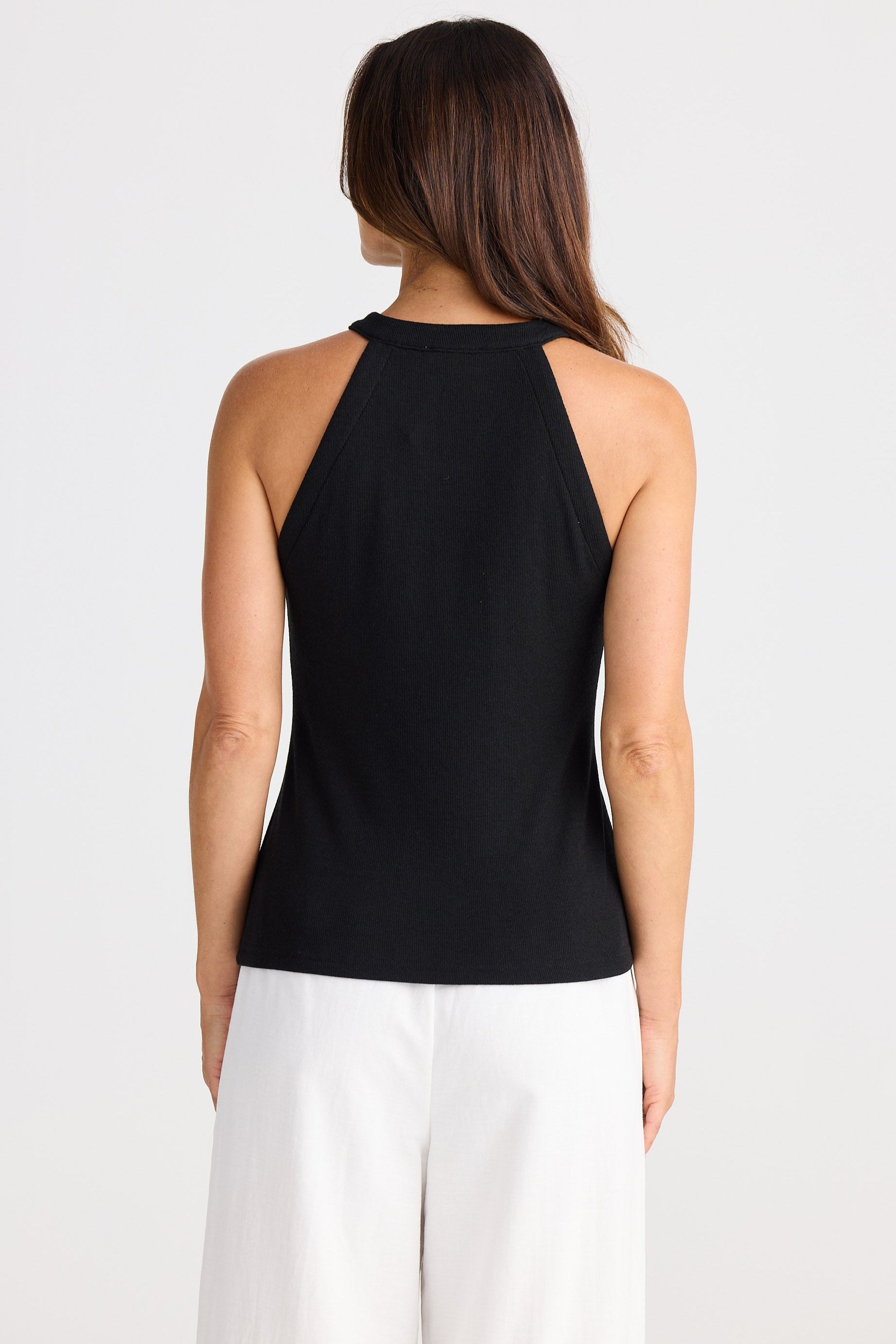 Woman wearing a black sleeveless top and white pants on a white background