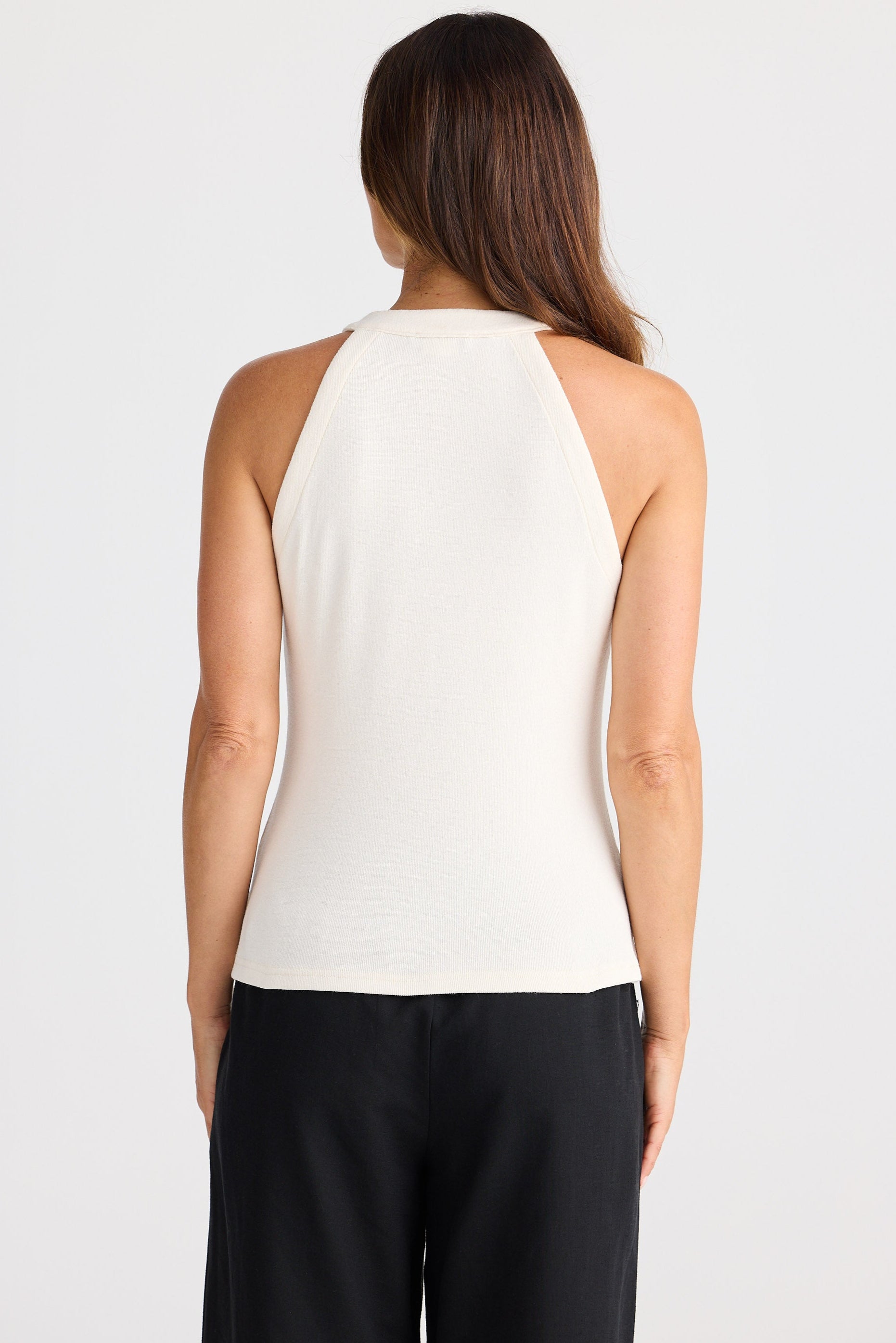 Woman wearing a white sleeveless top and black pants on a light gray background