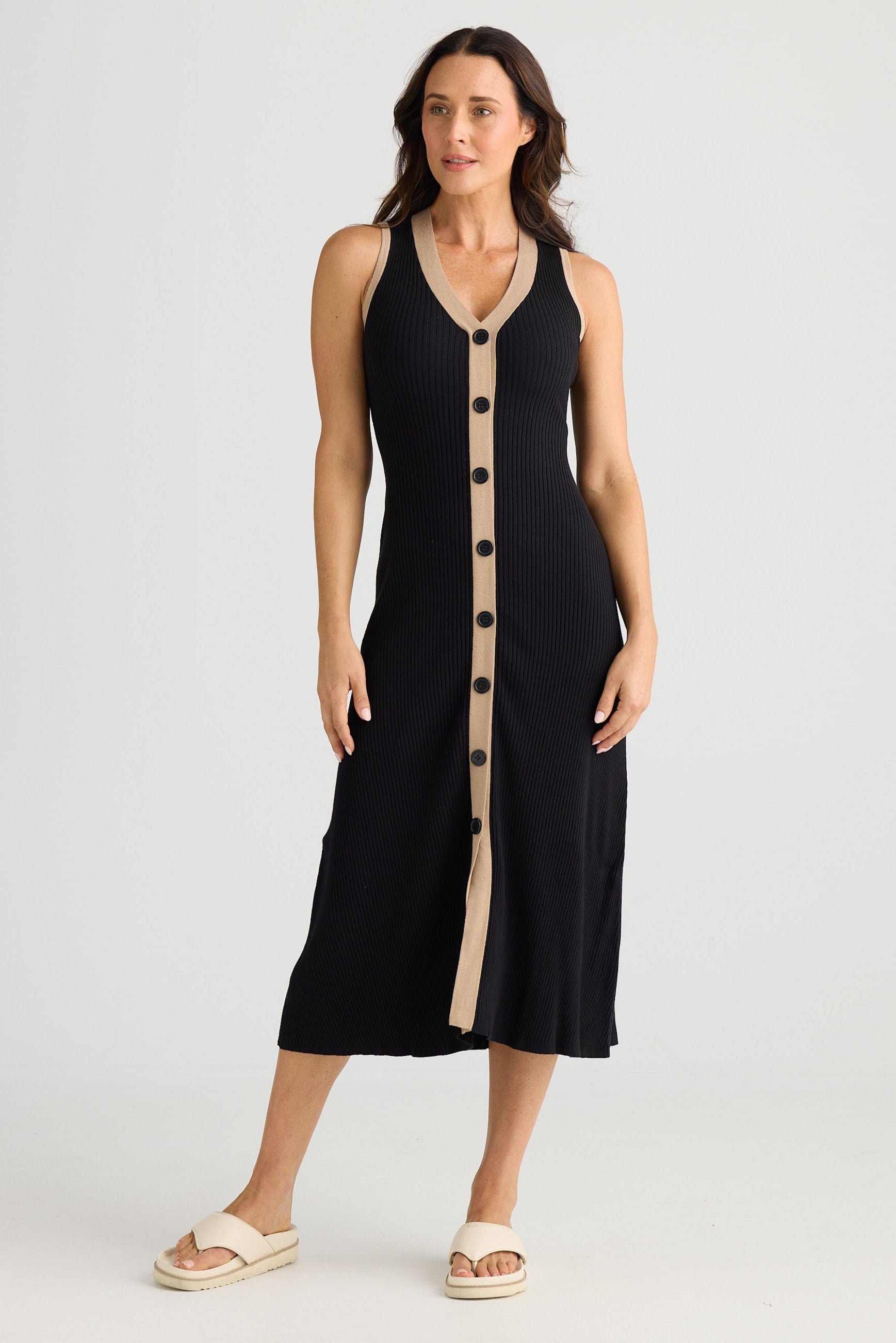 Woman wearing a black sleeveless dress with beige buttons on a white background