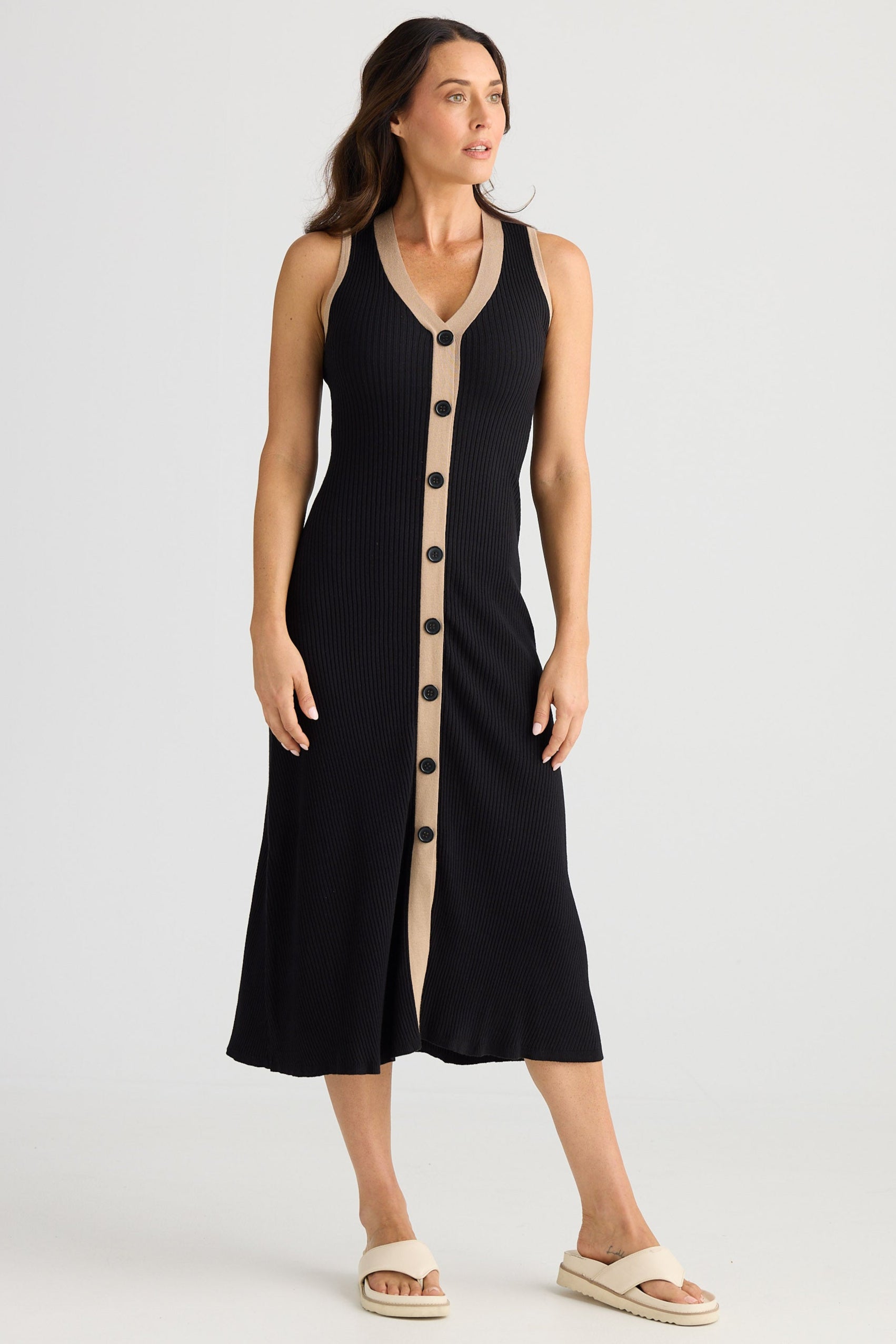 Woman wearing a black sleeveless dress with button details on a white background