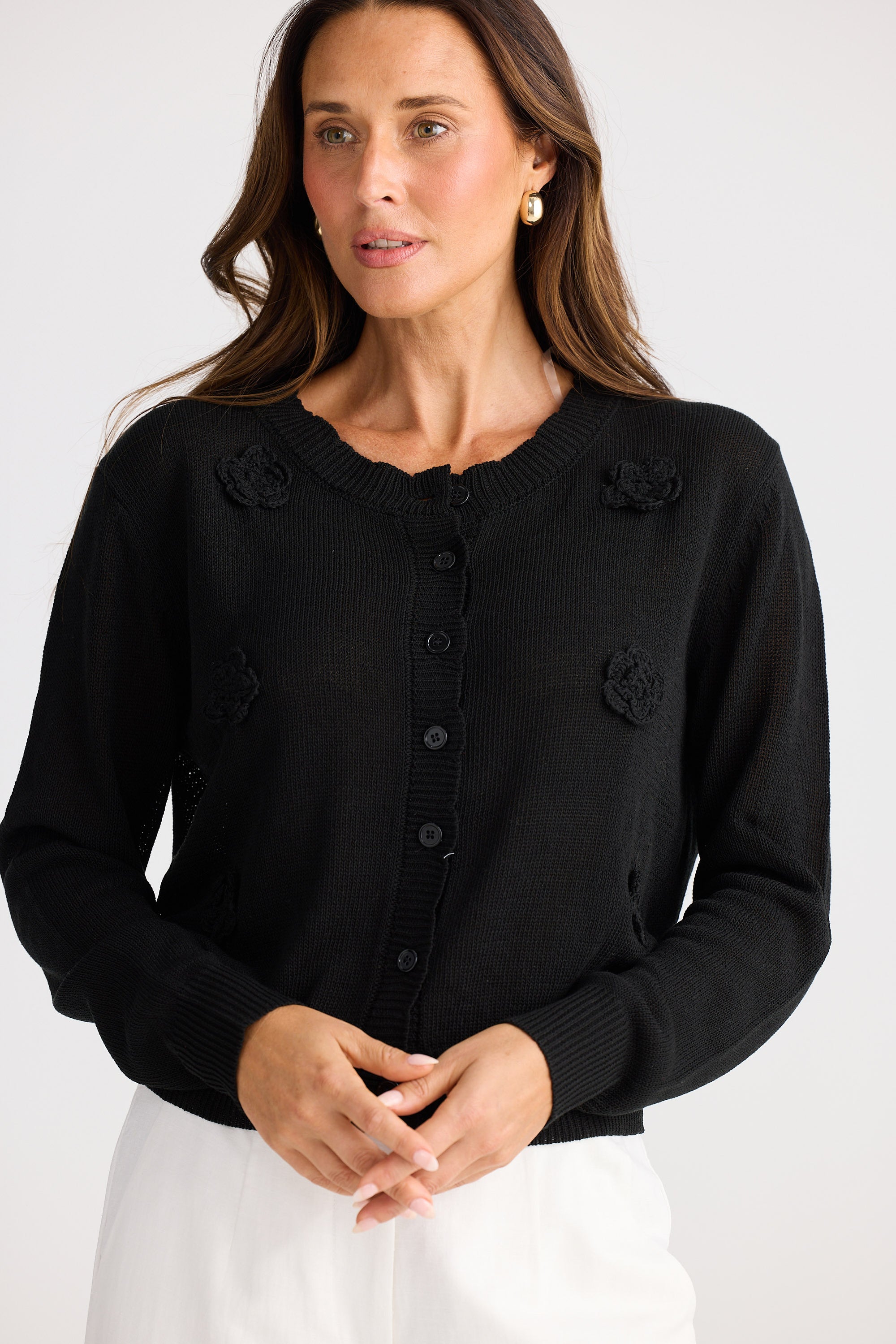 Woman wearing a black cardigan with floral embellishments on a white background