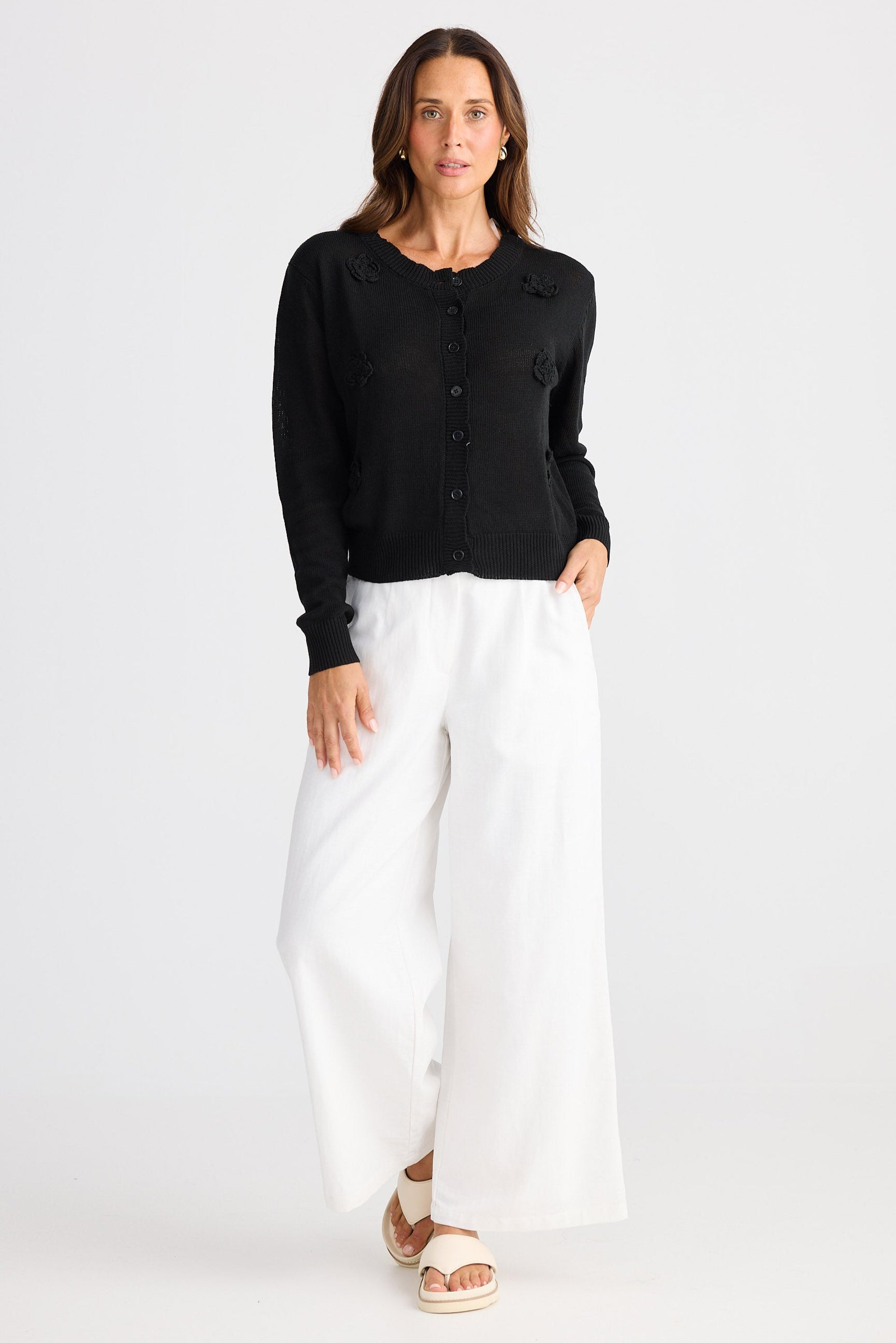 Woman wearing a black cardigan and white pants on a white background