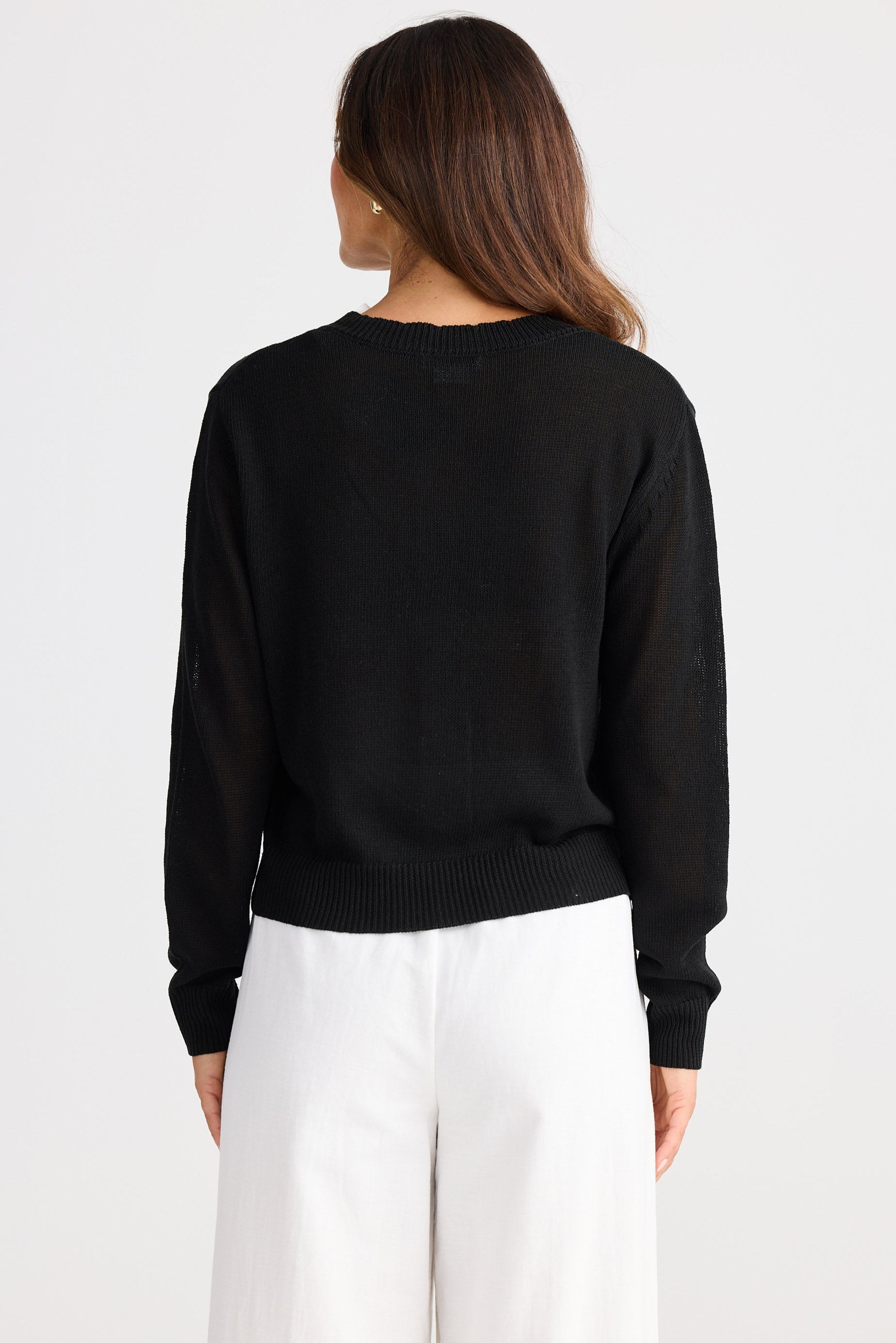 Person wearing a black sweater and white pants on a plain background