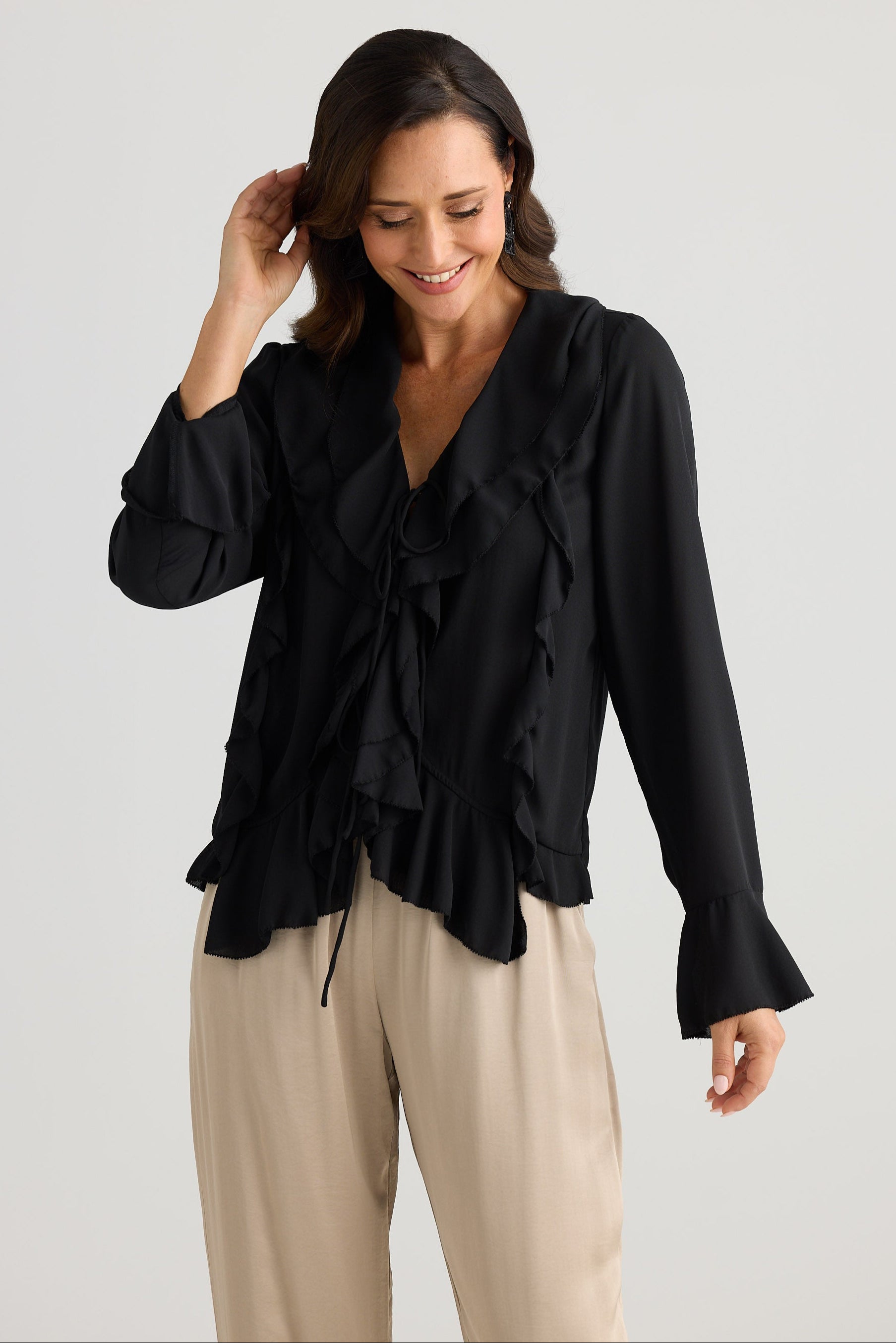Woman wearing a black blouse with ruffled details and beige pants on a light gray background