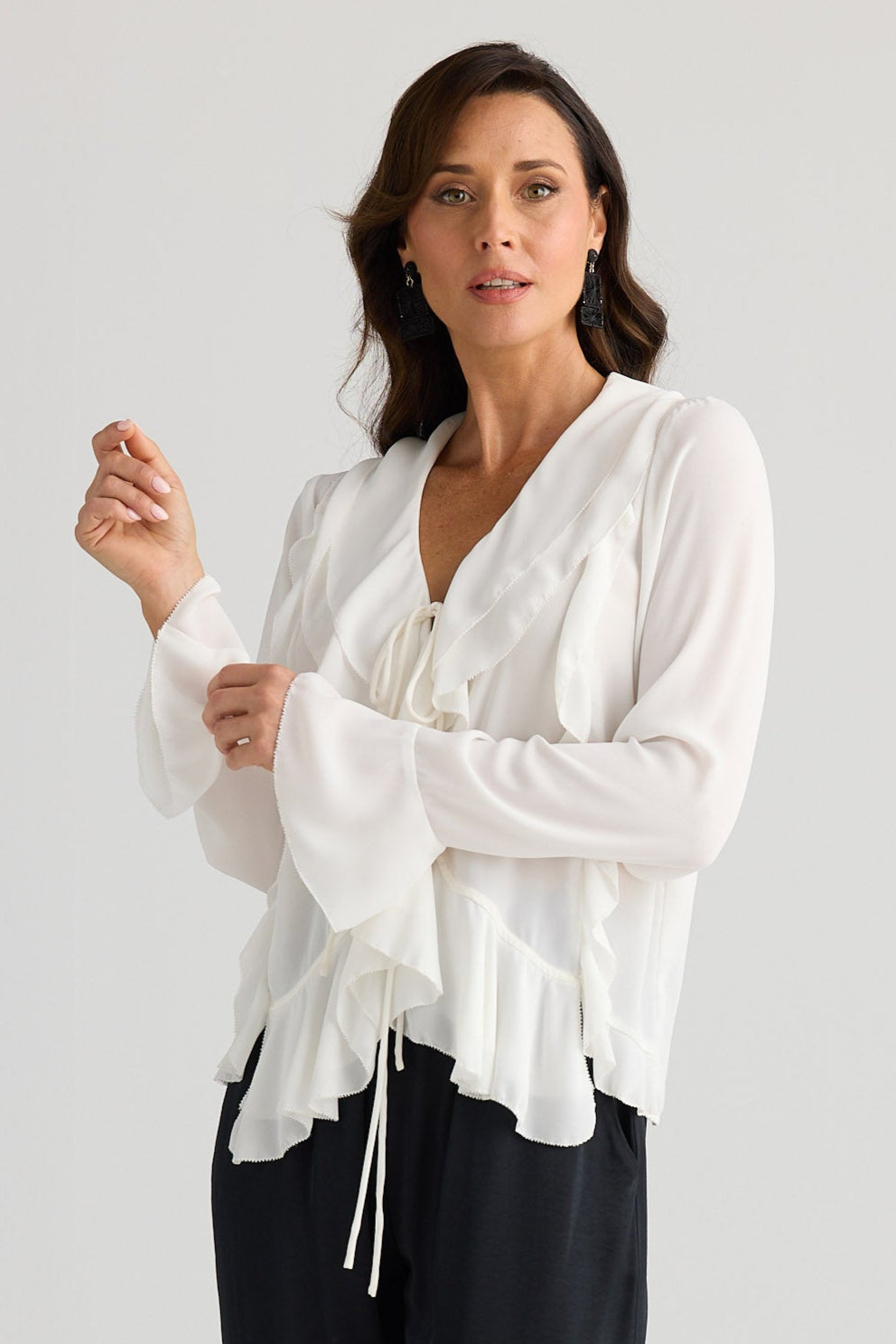 Woman wearing a white blouse and black pants on a light gray background