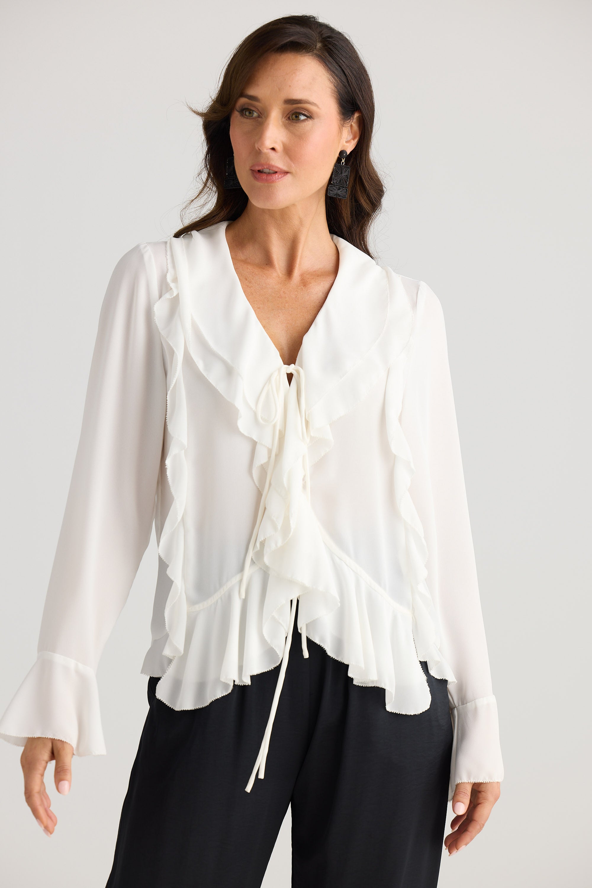 Woman wearing a white blouse with ruffled details on a plain background