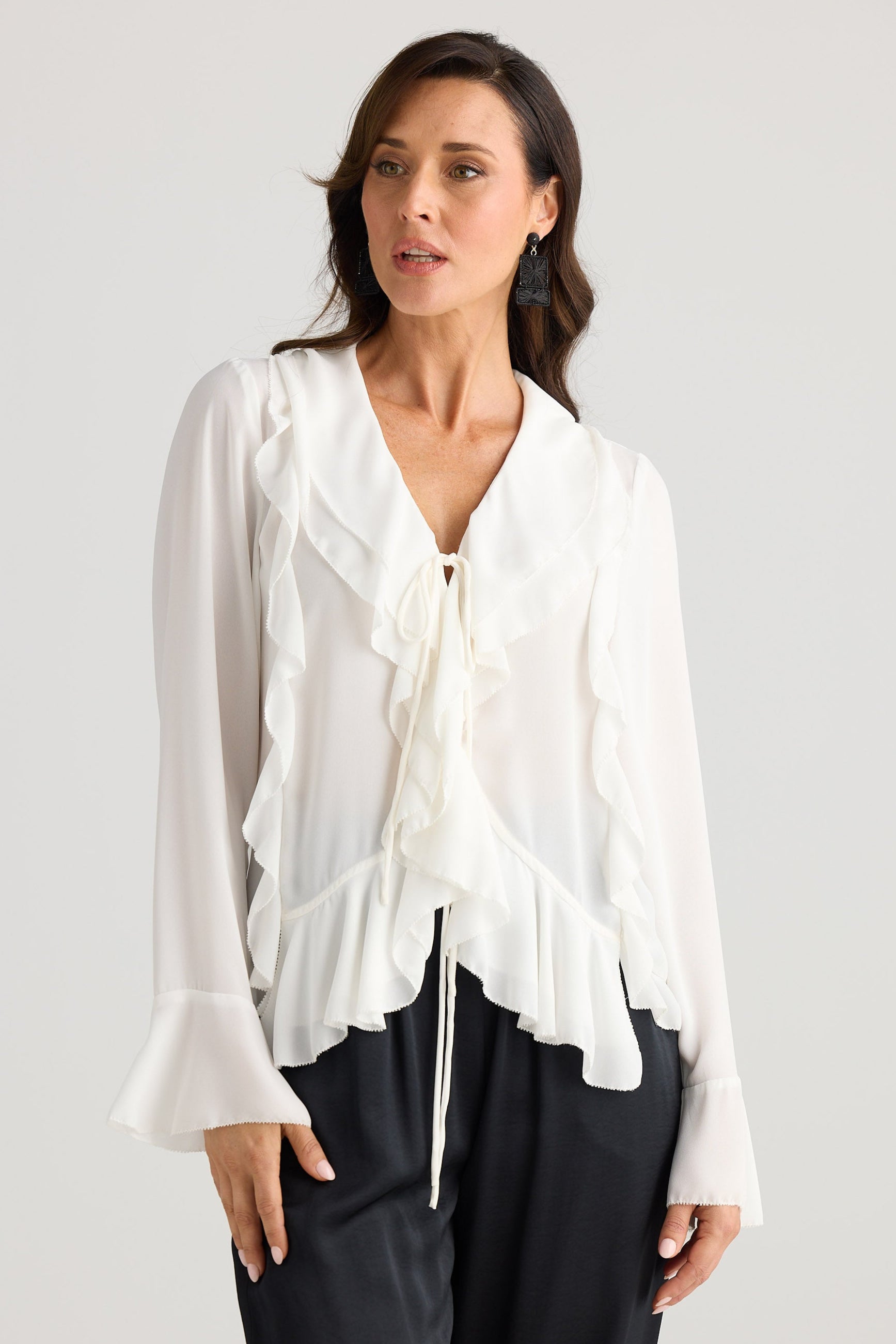 Woman wearing a white blouse with long sleeves and black pants on a light gray background
