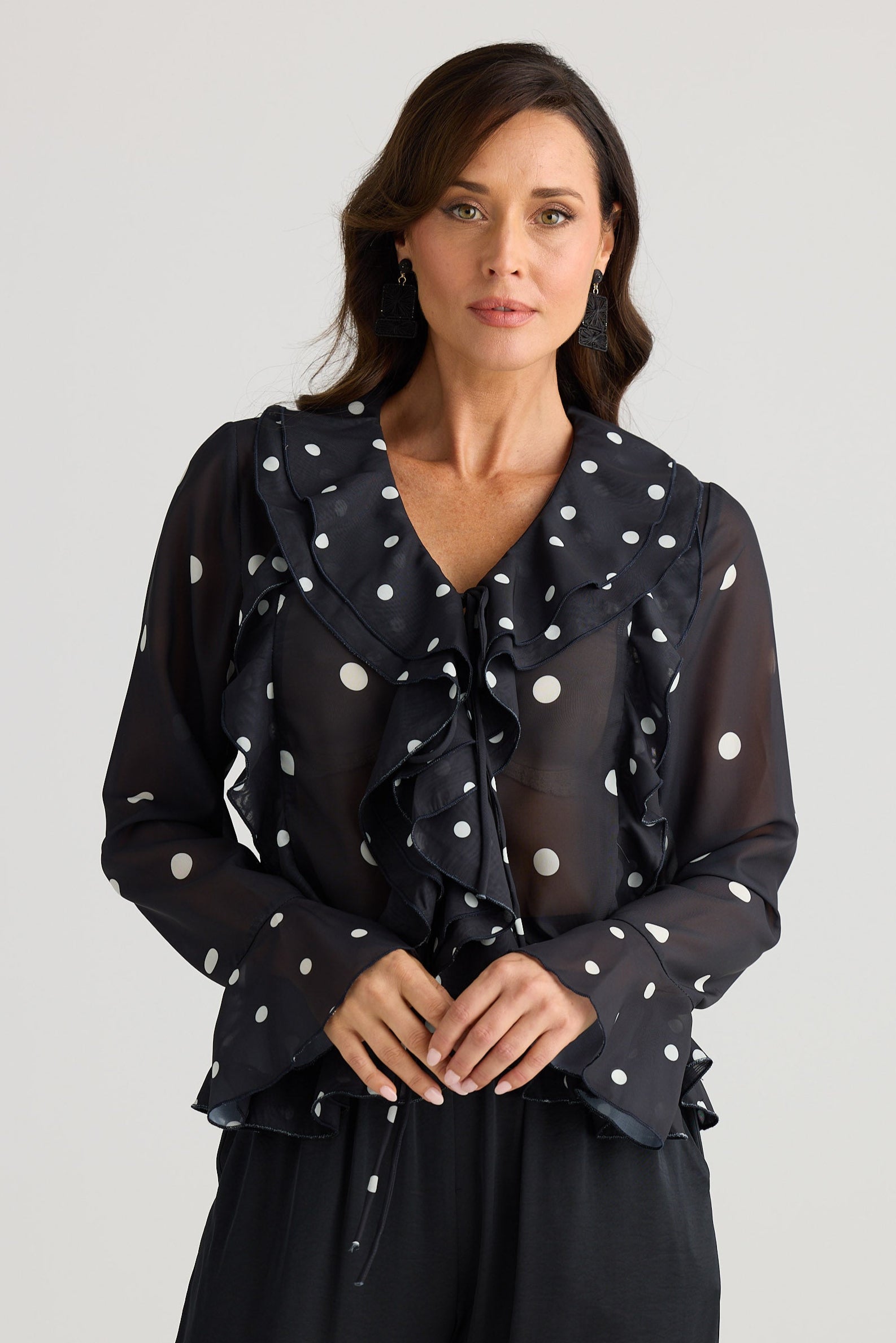 Woman wearing a black blouse with white polka dots and black pants on a light gray background