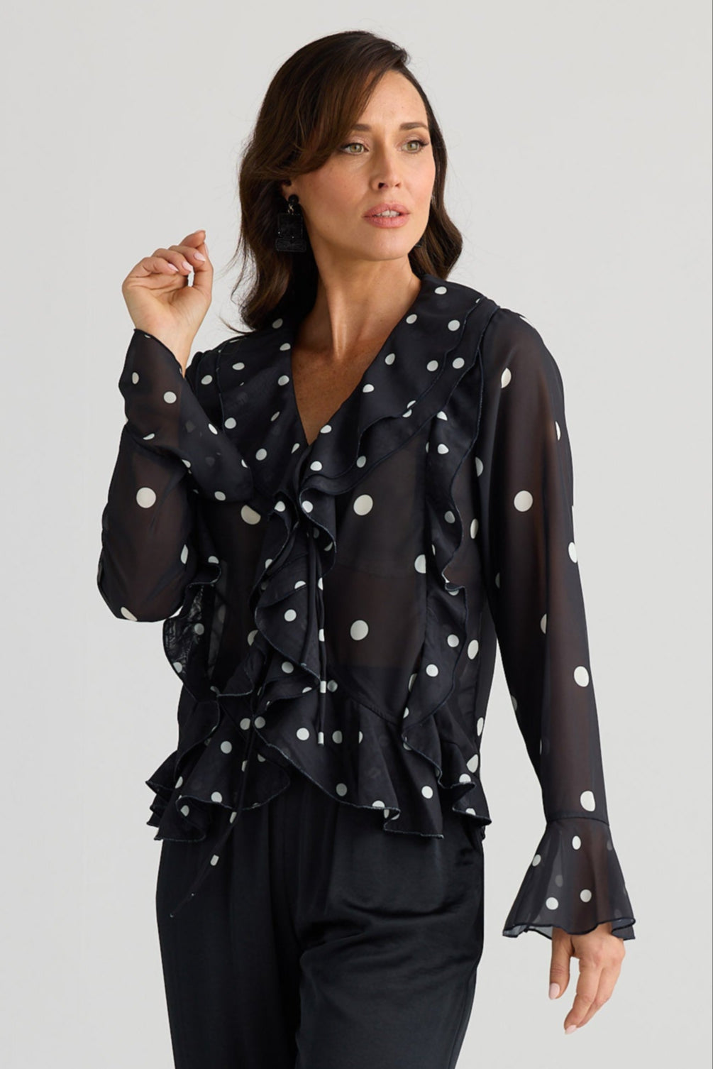 Woman wearing a black blouse with white polka dots and black pants on a white background